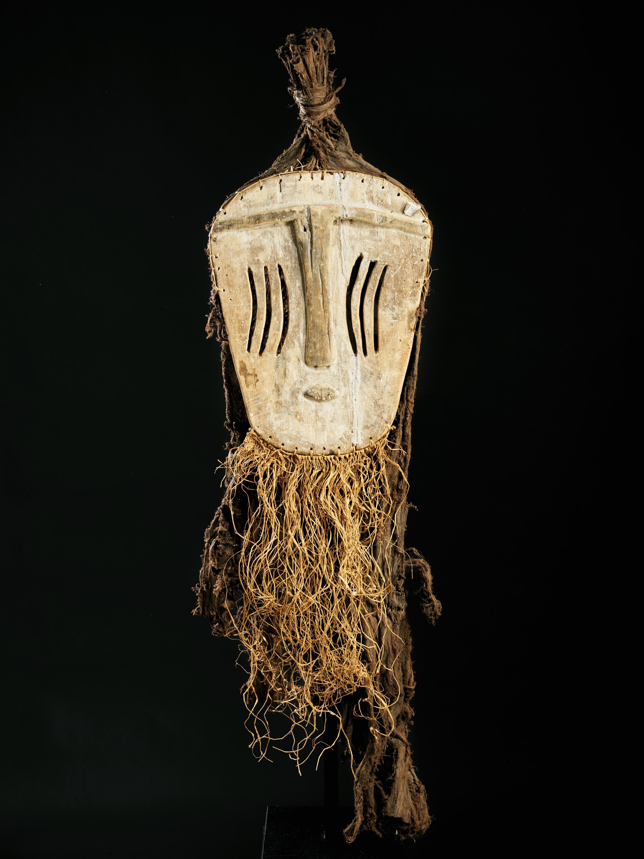 Ce masque rare, de forme presque circulaire, appartient à la société secrète Ekanga et aurait été conservé dans des paniers au cœur de leurs sanctuaires. Le style minimaliste et les pigments blancs indiquent le travail d'un artiste mbole. Le recto