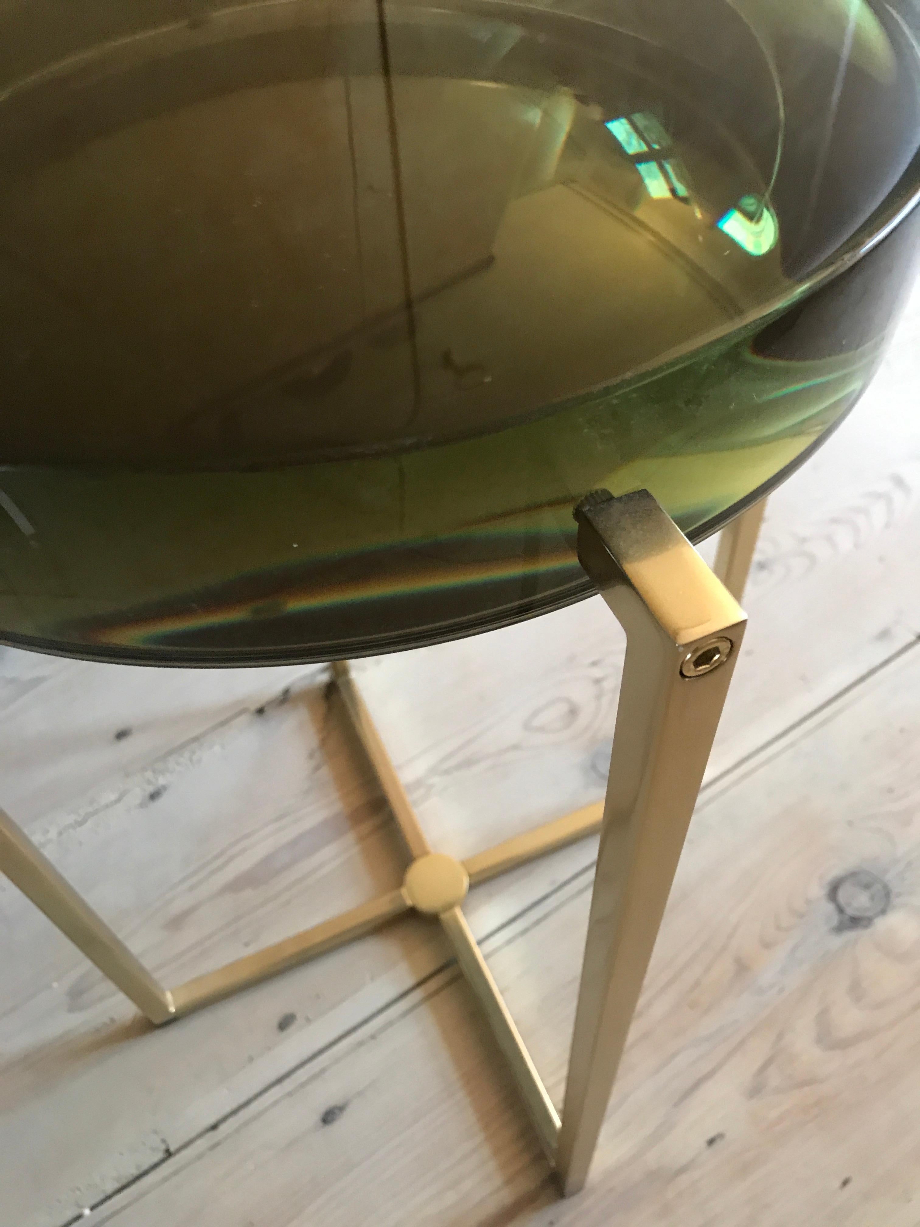Lens table with bottle green tinted resin top backed by acrylic mirror on brass base.