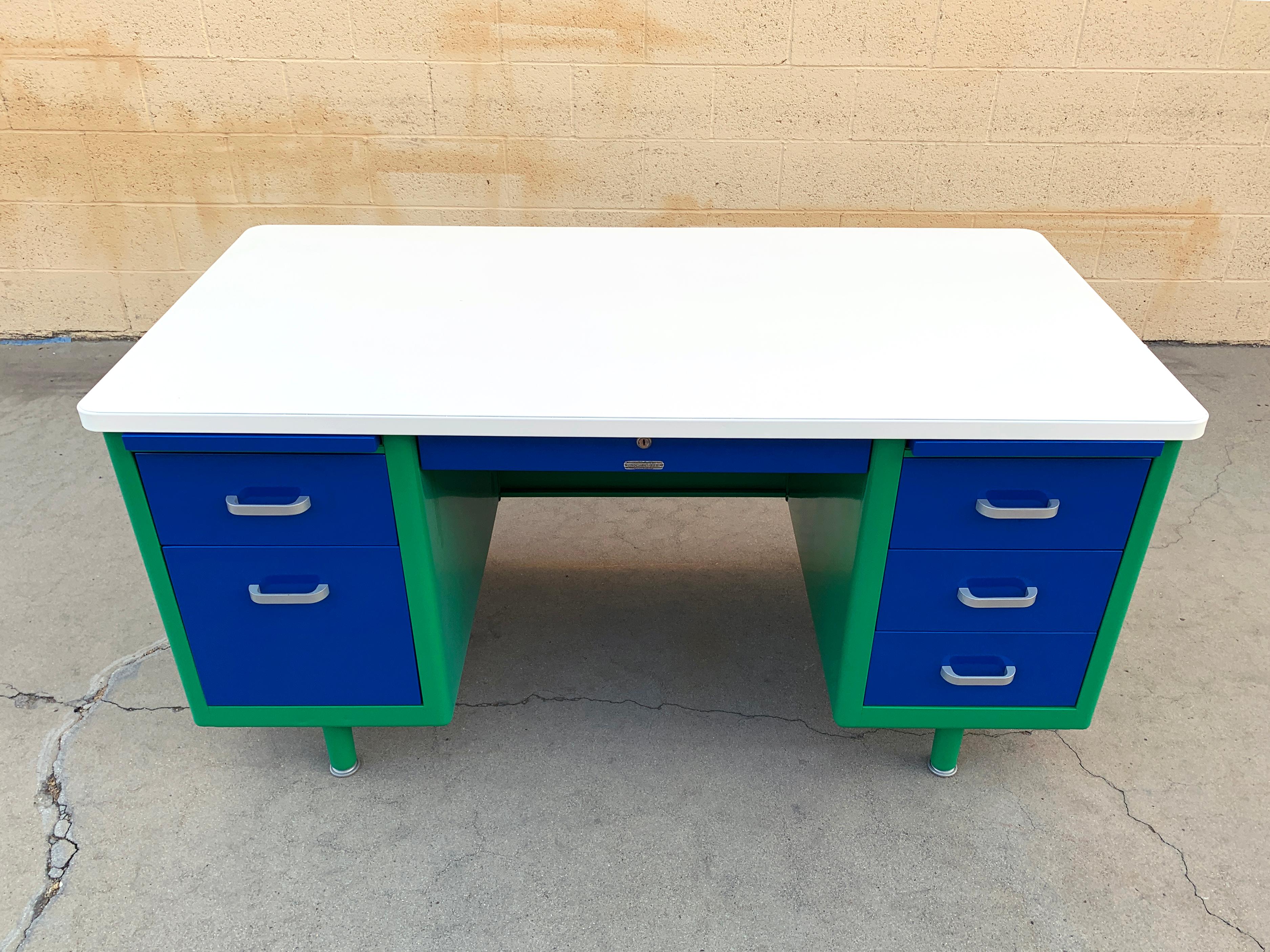 In stock and ready to ship!

Classic 1960s McDowell Craig tanker desk refinished in a playful Bauhaus-inspired color combination of green and blue with a while top. 

This Classic double pedestal desk features many utility drawers, one filing