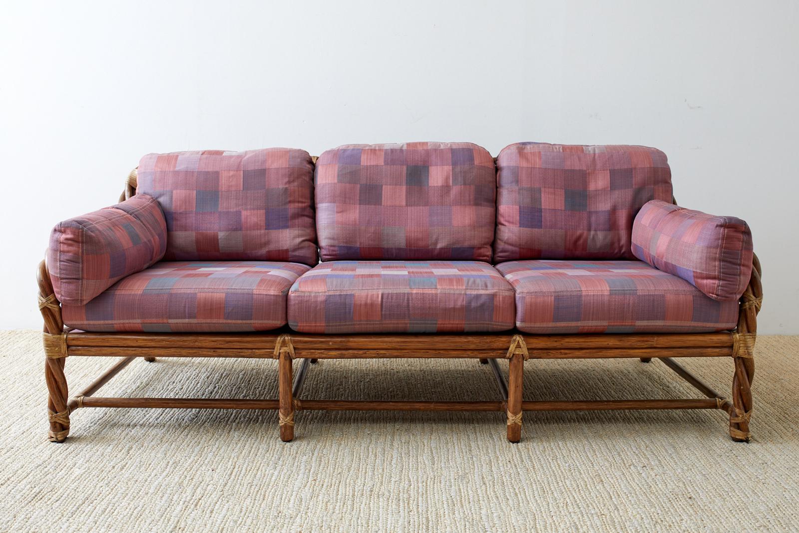 Distinctive bamboo rattan sofa made by McGuire in the California organic modern style. Features a twisted, bent rattan back that gracefully curves down the arms to the front legs. Lashed together with an abundance of leather rawhide laces in a light