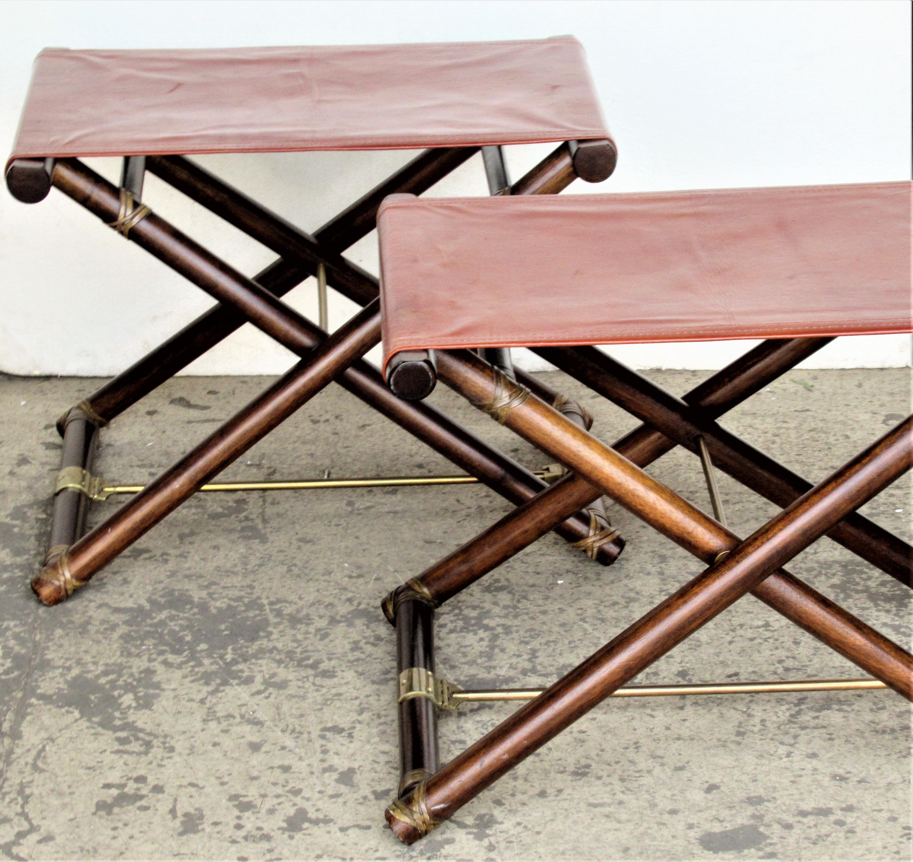 A matched pair of folding collapsible X-form campaign directors stools / ottomans by McGuire. Bamboo wood bases / rawhide bindings / brass fittings and stretchers, stitched leather seats. Brass tags - McGuire San Fancisco /paper labels - Made by the