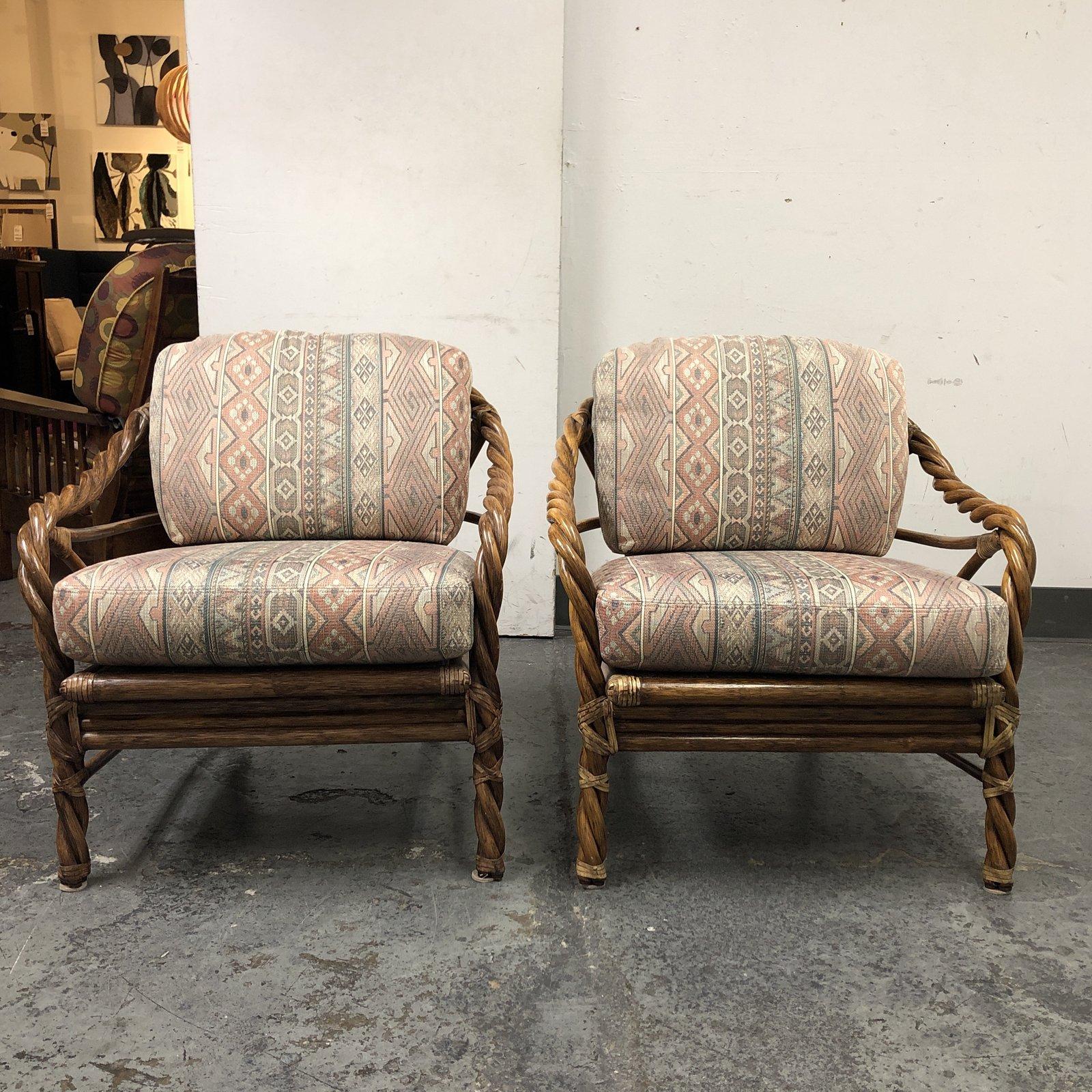 It presents a pair of mid-20th century twisted arm lounge chairs by McGuire. Made of twisted and bent rattan woods, wrapped and joined with rawhide. The back and seat cushions are loose and foam based, upholstered in a tribal inspired fabric.