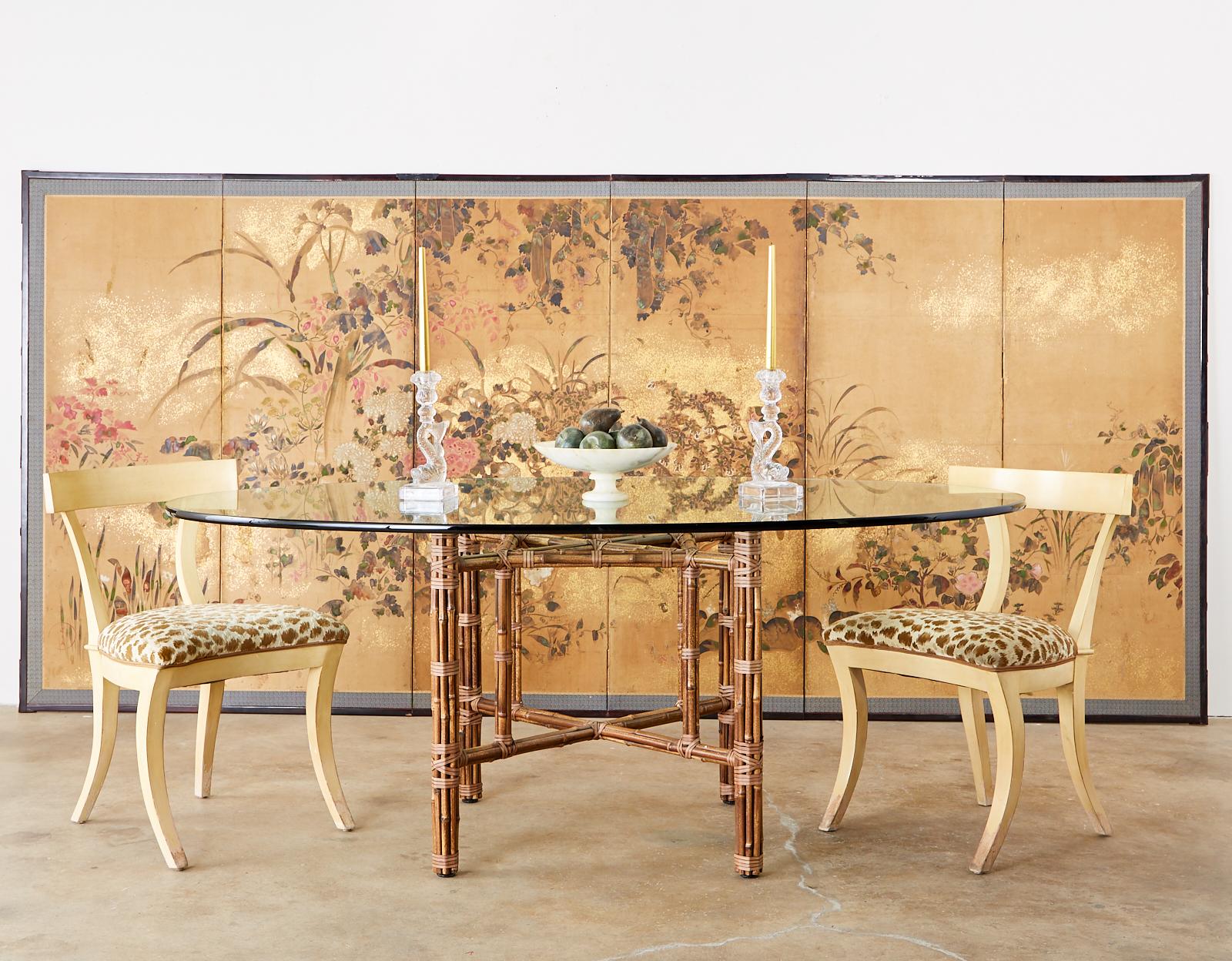 Genuine McGuire California organic modern style oval dining table constructed from an authentic Golden Gate Bridge orange painted iron frame covered with bamboo rattan poles. The rattan is lashed together with leather rawhide laces and each leg has