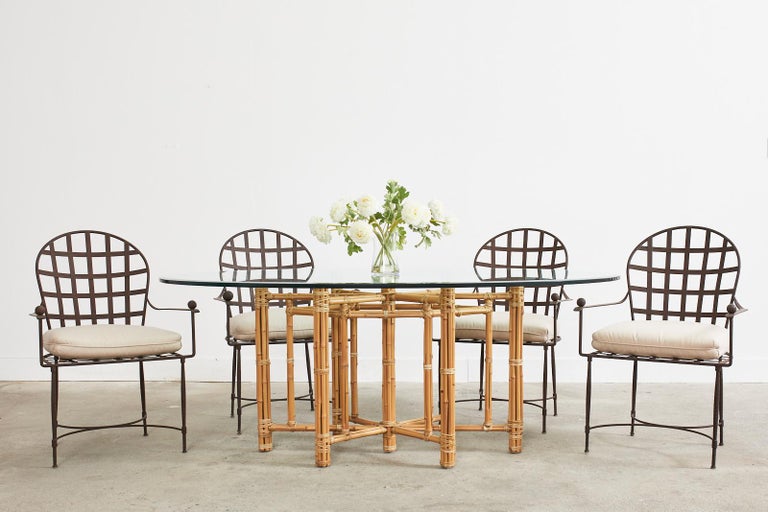 Stunning organic modern oval dining table made by McGuire. The table features an elongated hexagonal star shaped base topped with a thick pane of McGuire oval, beveled glass. The geometric base has an iron frame wrapped with blonde-toned bamboo