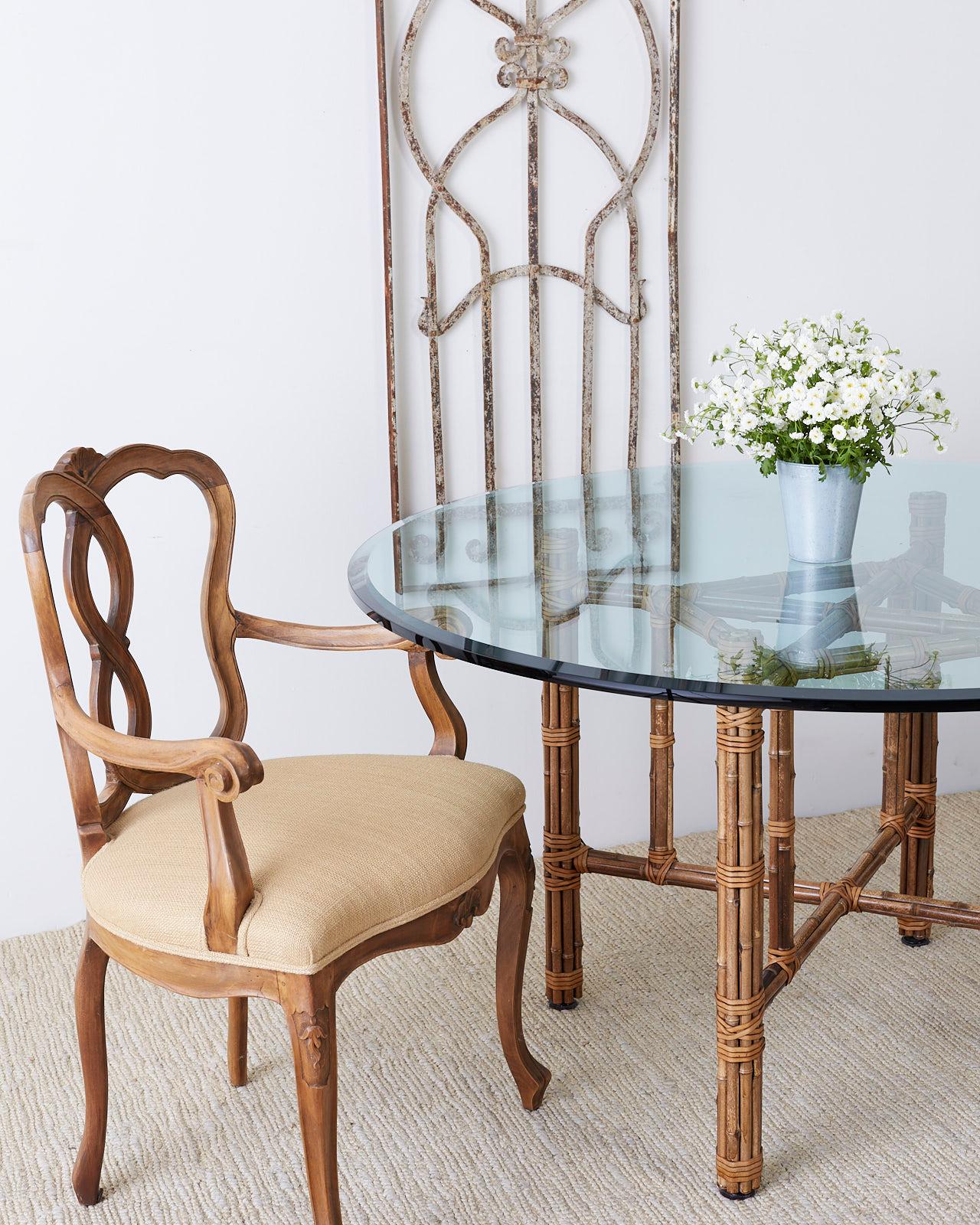 Genuine McGuire organic modern style dining table constructed from an iron frame hand wrapped with bamboo rattan poles. Reinforced with McGuire's signature leather rawhide strapping laces. The square base is topped with a thick round beveled glass