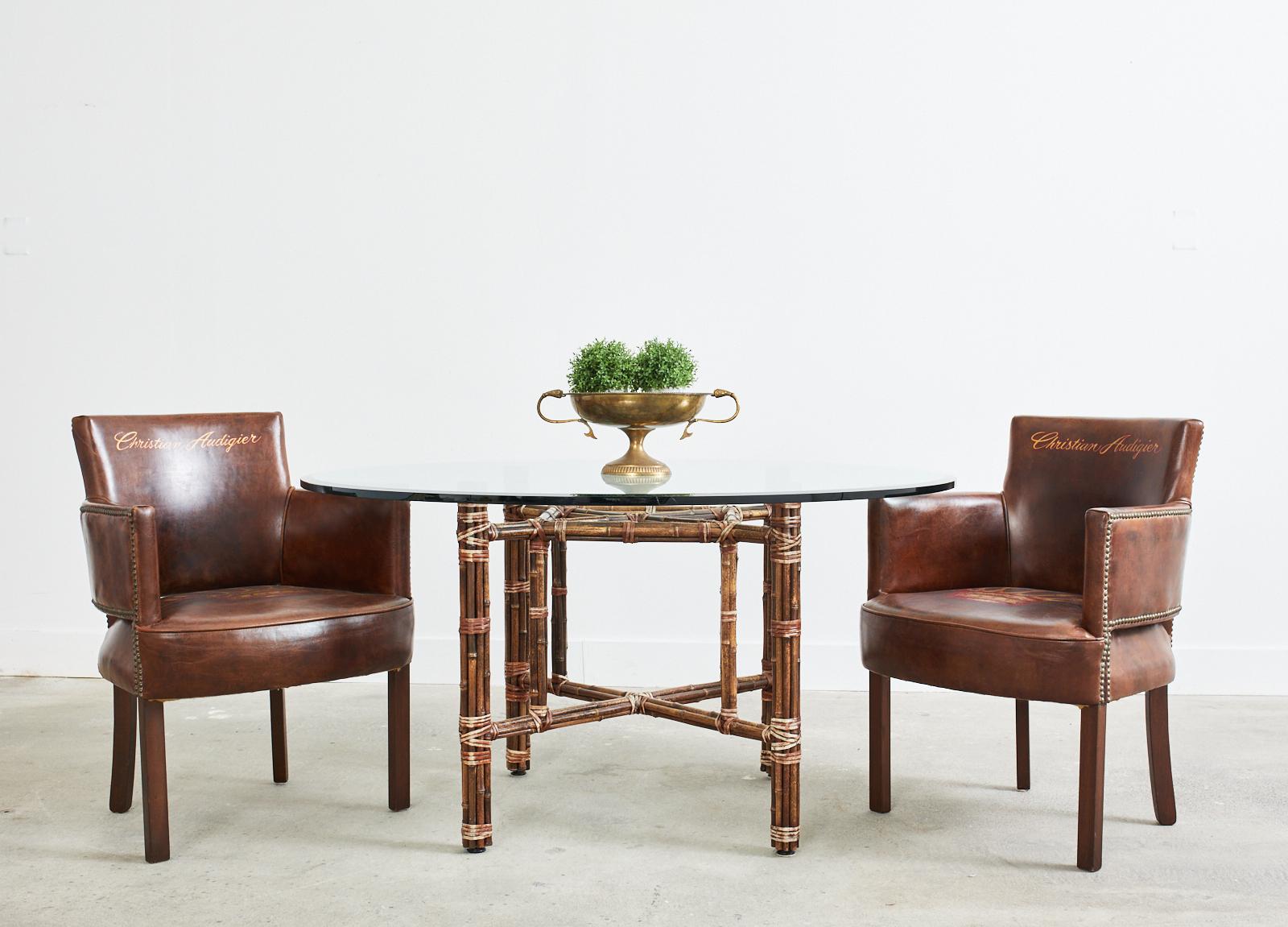 Genuine McGuire round dining table featuring a square base. The base is created from an iron frame painted golden gate orange for authencity and completely wrapped with bamboo rattan poles lashed together with leather rawhide laces. The base