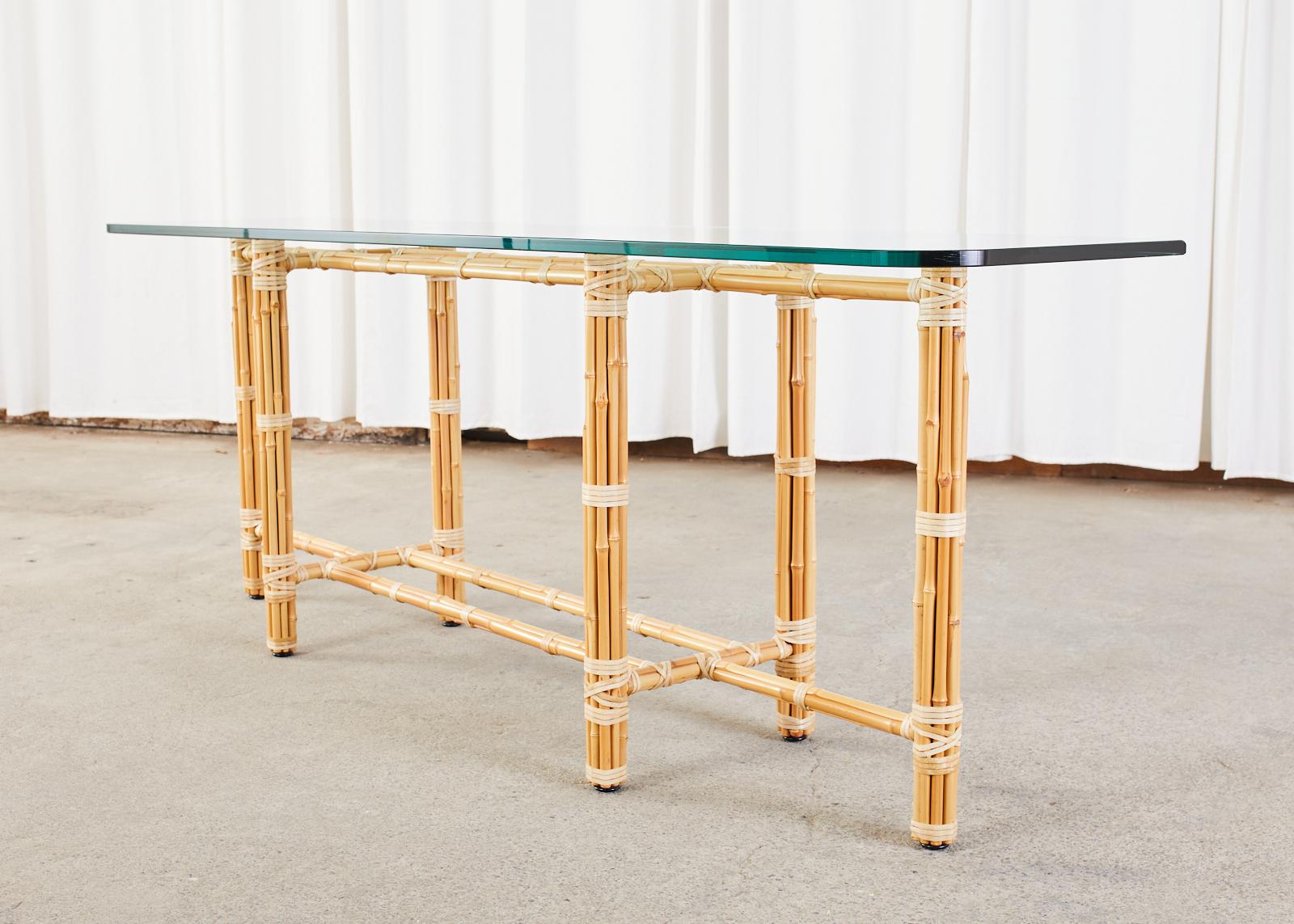 Elongated McGuire console table or sofa table made in the California organic modern style. The long rectangular table features an iron base wrapped with blonde bamboo poles lashed together with leather rawhide laces topped with a very thick pane of