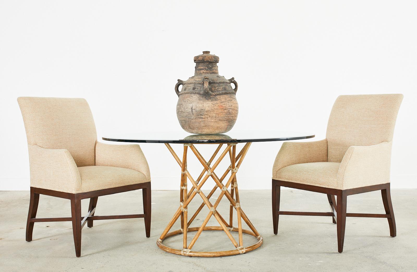 Gorgeous organic modern glass top dining table or center table made by McGuire. The table features a bamboo rattan pedestal base with a waisted hourglass form. Constructed from two rattan rings conjoined by criss-cross rattan poles lashed together