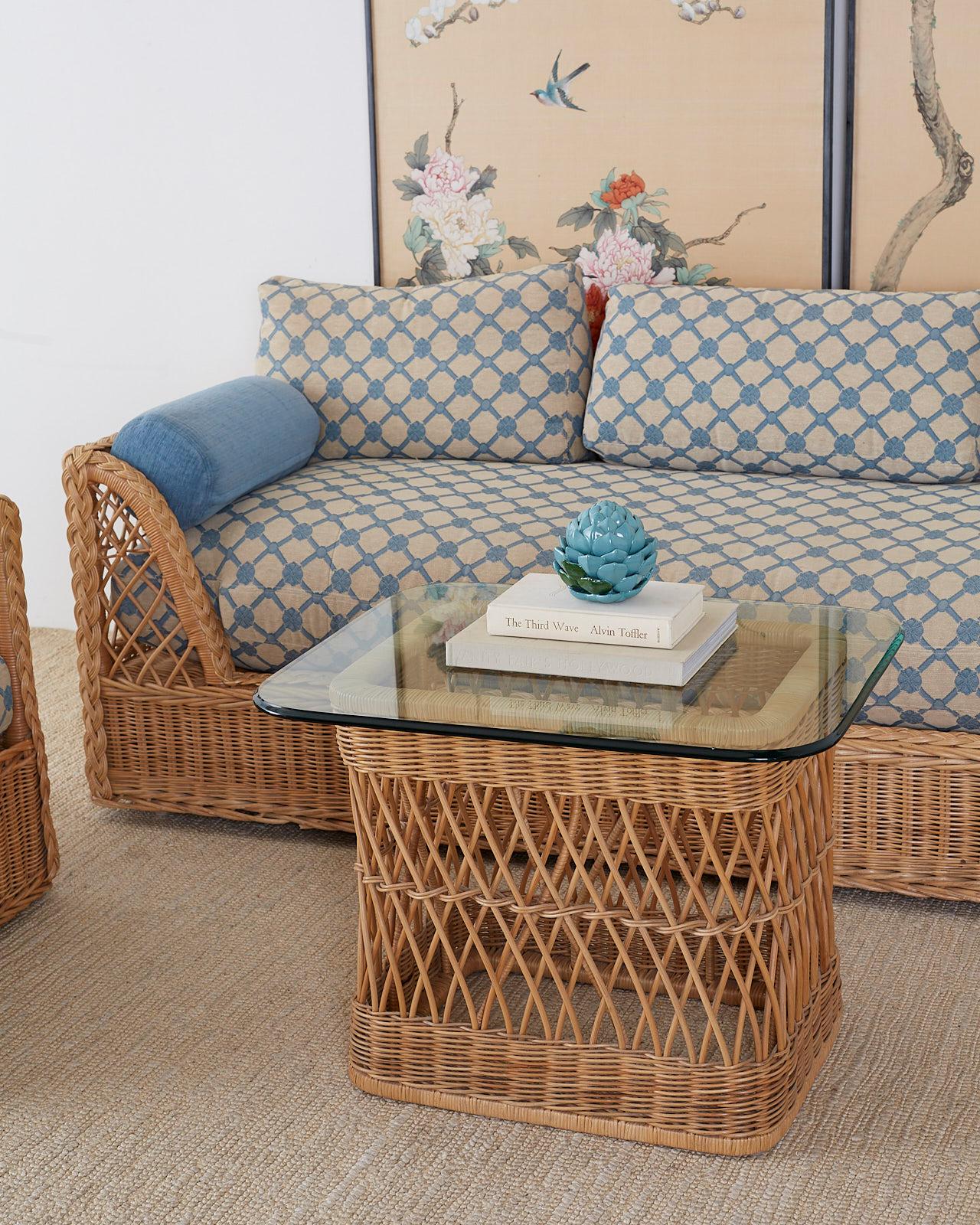 Organic modern style coffee cocktail table made by McGuire featuring a woven rattan wicker frame topped with a thick pane of glass. The glass top has rounded corners and an ogee edge. The base has a decorative open fretwork geometric design grounded