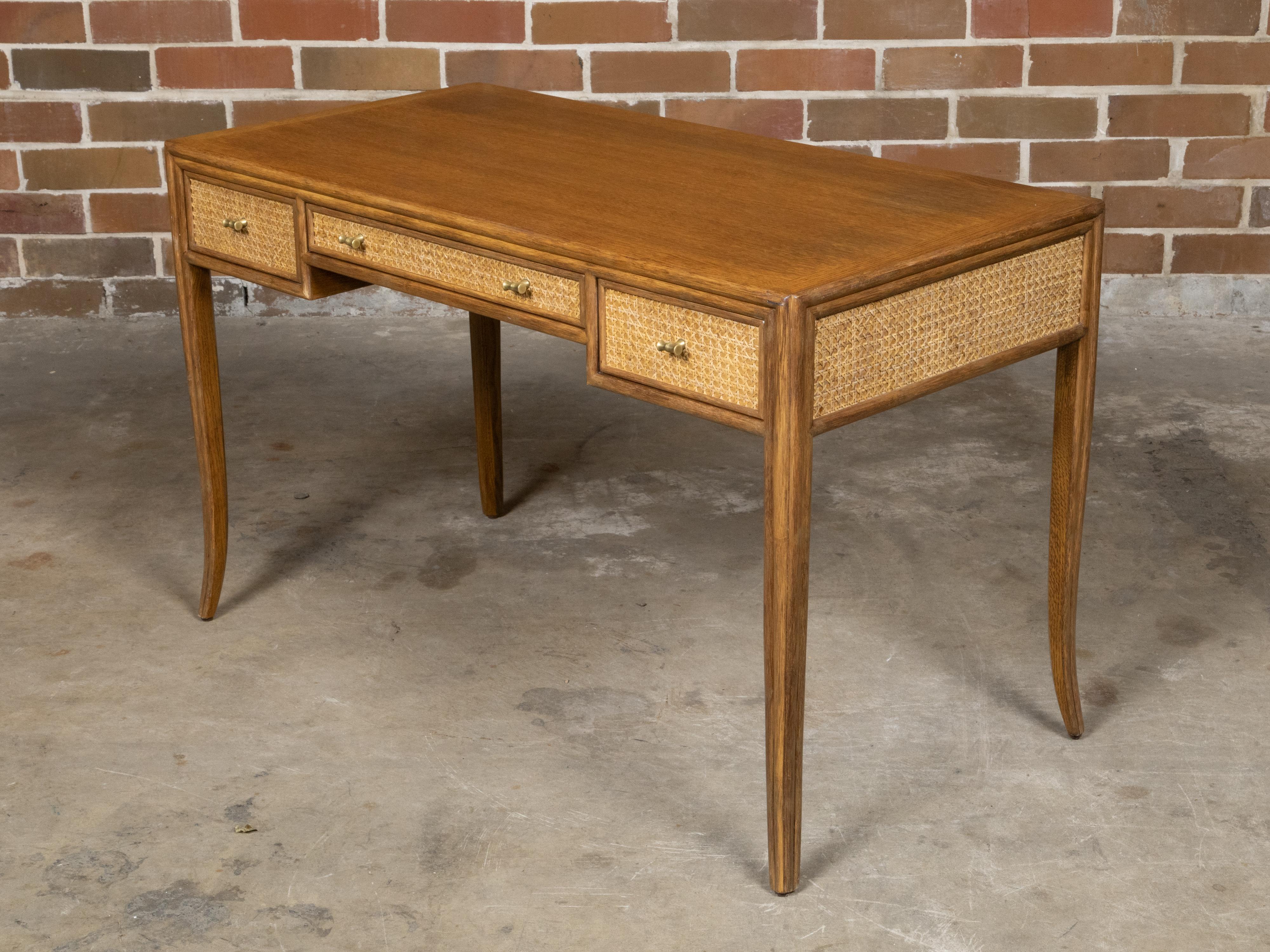 A McGuire rattan and oak writing desk from the Midcentury period, with three drawers and saber legs. This exquisite McGuire rattan and oak writing desk from the Midcentury period embodies the perfect blend of natural materials and refined