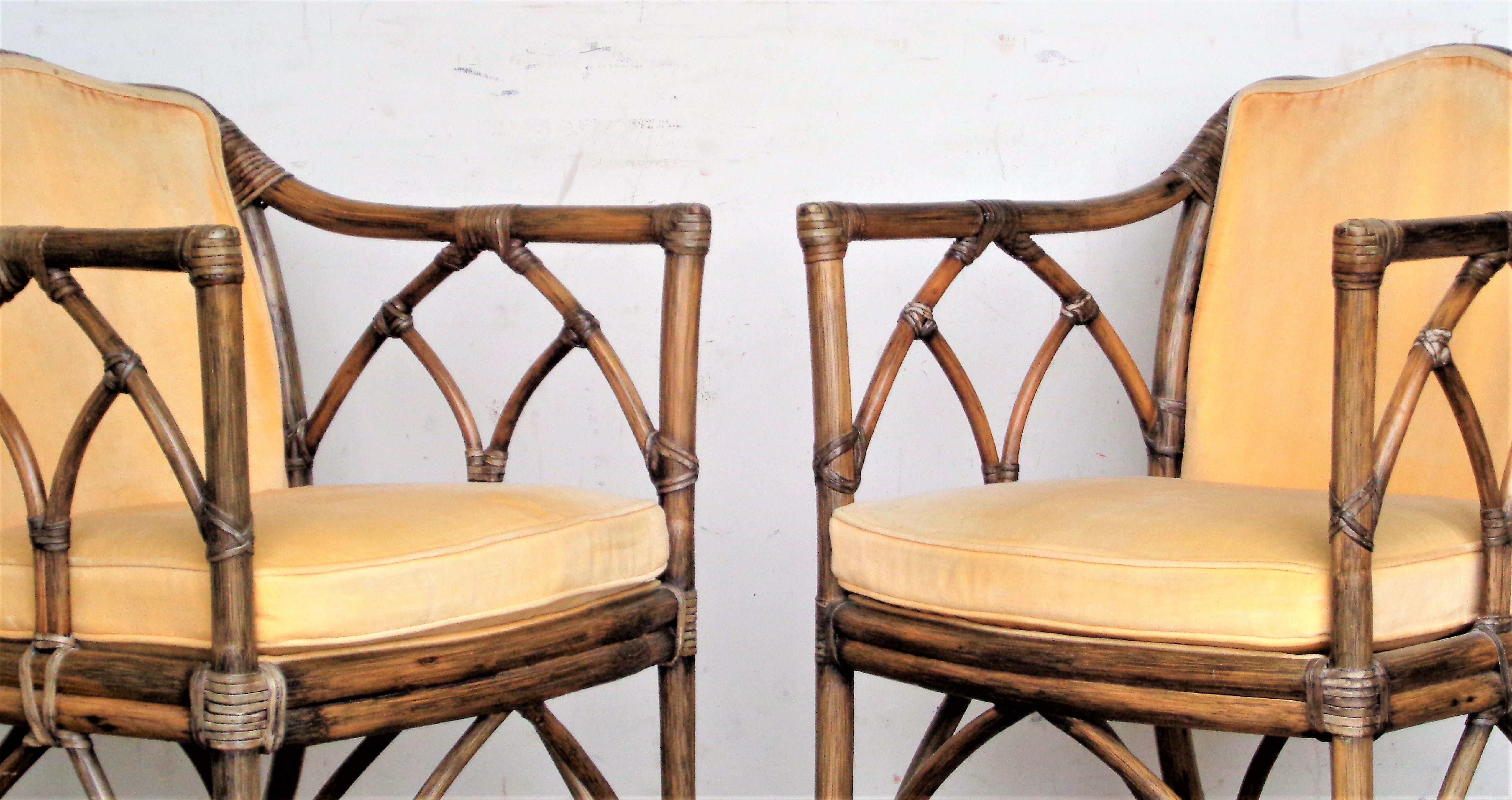 A pair of McGuire rattan armchairs / lounge chairs with cathedral design backs and arms, rawhide leather bindings, very good original finish, vintage soft velvet like upholstery. McGuire, San Francisco patent numbered brass tags on underside rail of