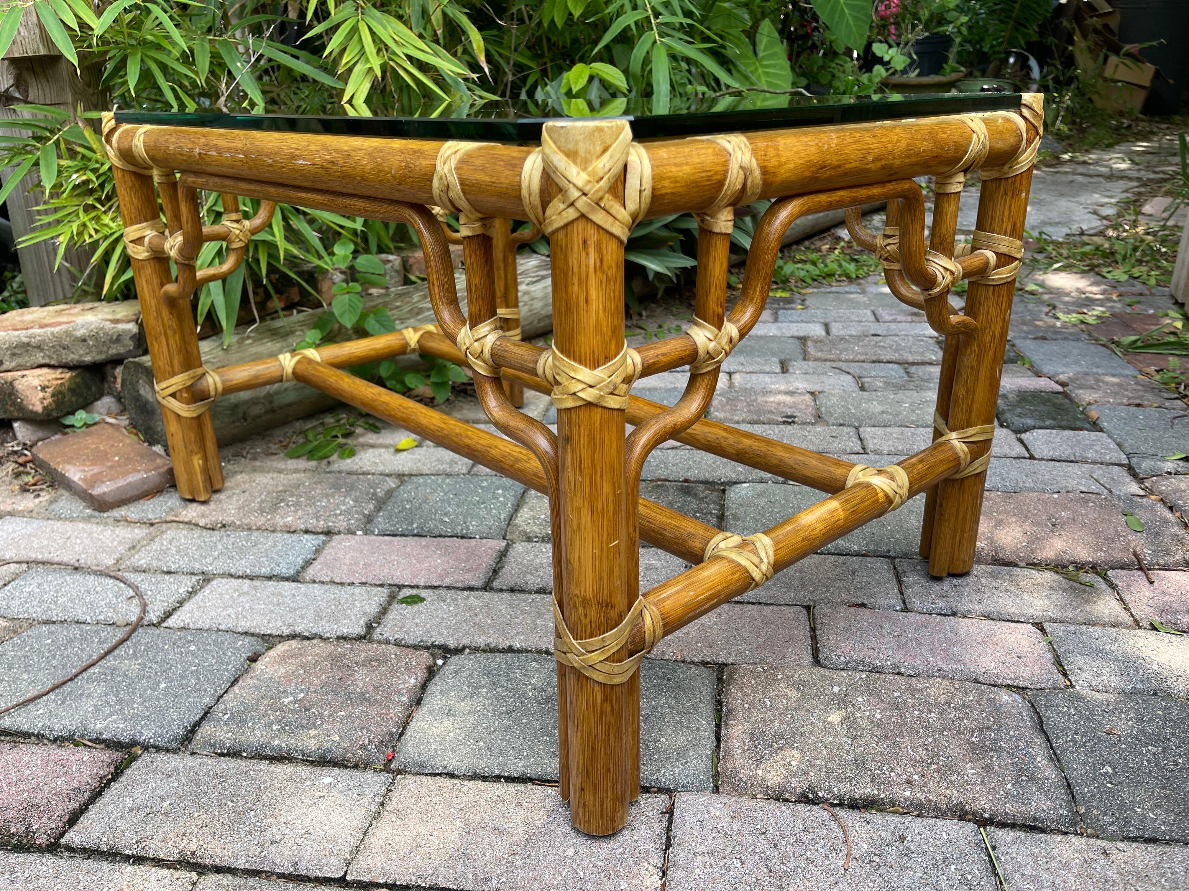 Striking handmade McGuire coffee table with fabulous fretwork detailing. Rattan with rawhide accents, thick glass top. Compact enough for a chic condo, or to complement a menagerie of coffee & cocktail tables in a larger space.