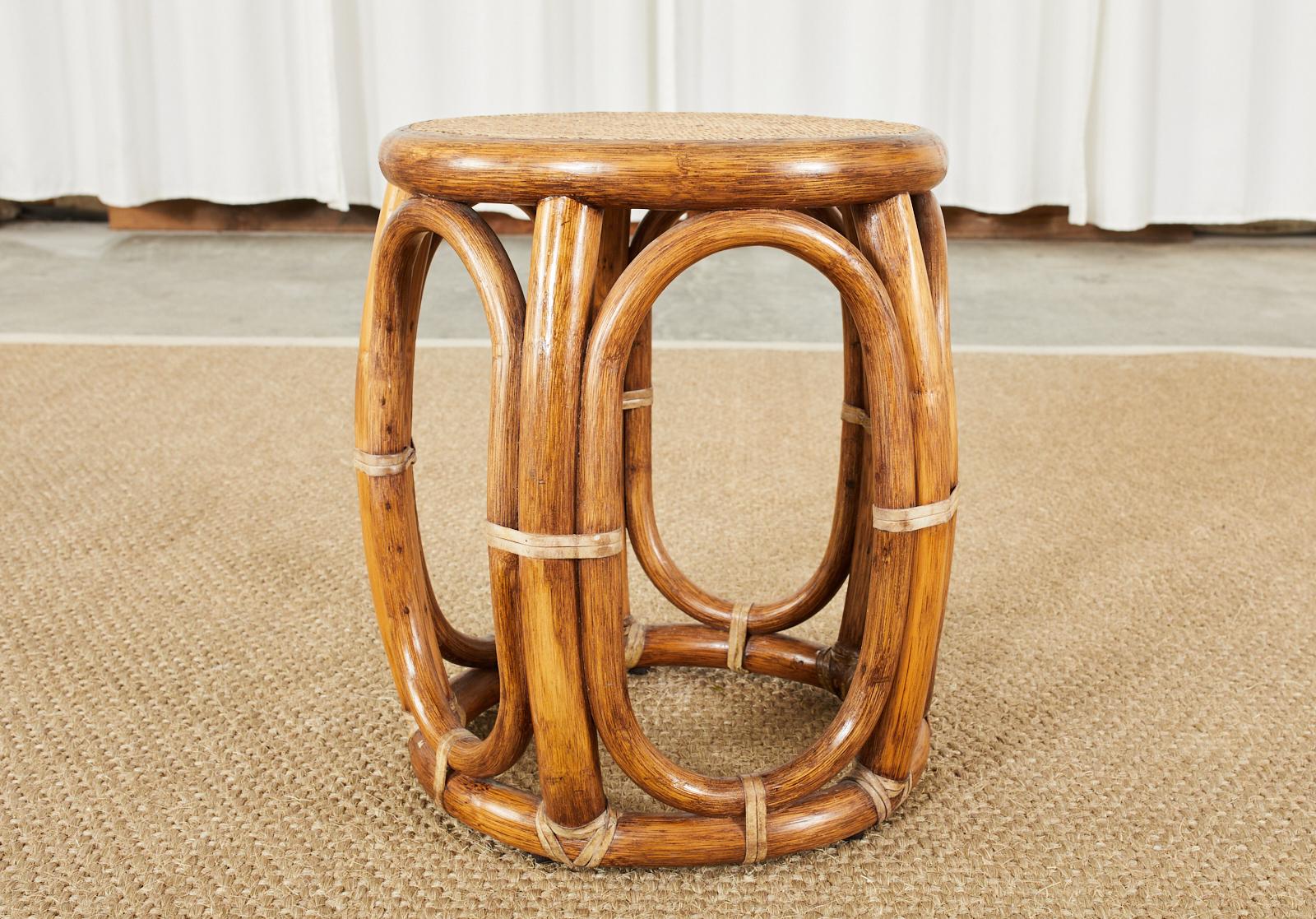 Organic modern style taboret drum formed stool or drink table made by McGuire. Crafted from a rattan frame with round ends conjoined by oval windows on the sides. The table features a woven grasscloth or raffia style wicker top that is inset.