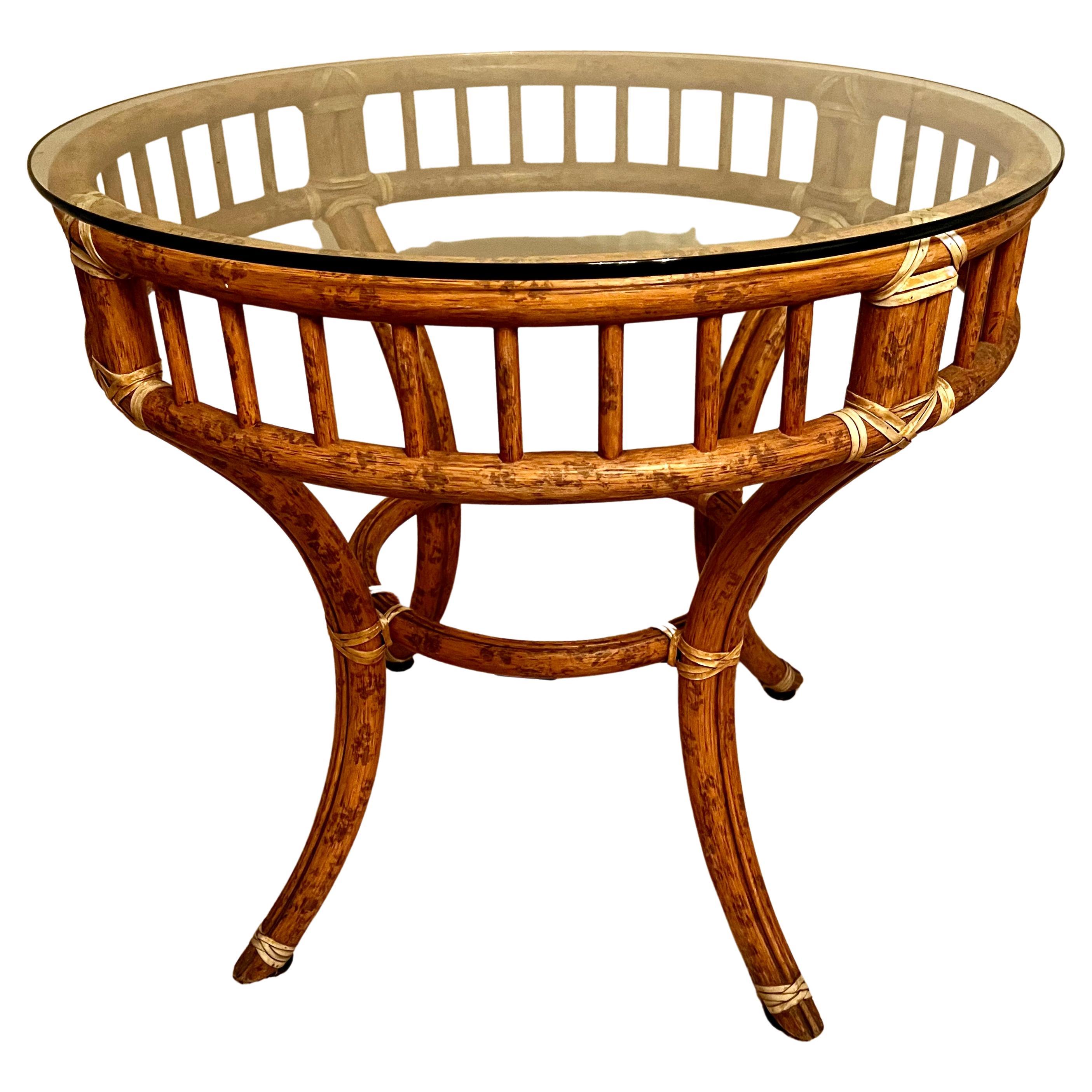Une table en rotin ou en bambou épais avec une sangle en cuir. La table ronde s'adapte à de nombreux espaces et peut être utilisée comme table d'appoint, table centrale ou, avec un verre plus grand, comme table de salle à manger pour quatre à huit