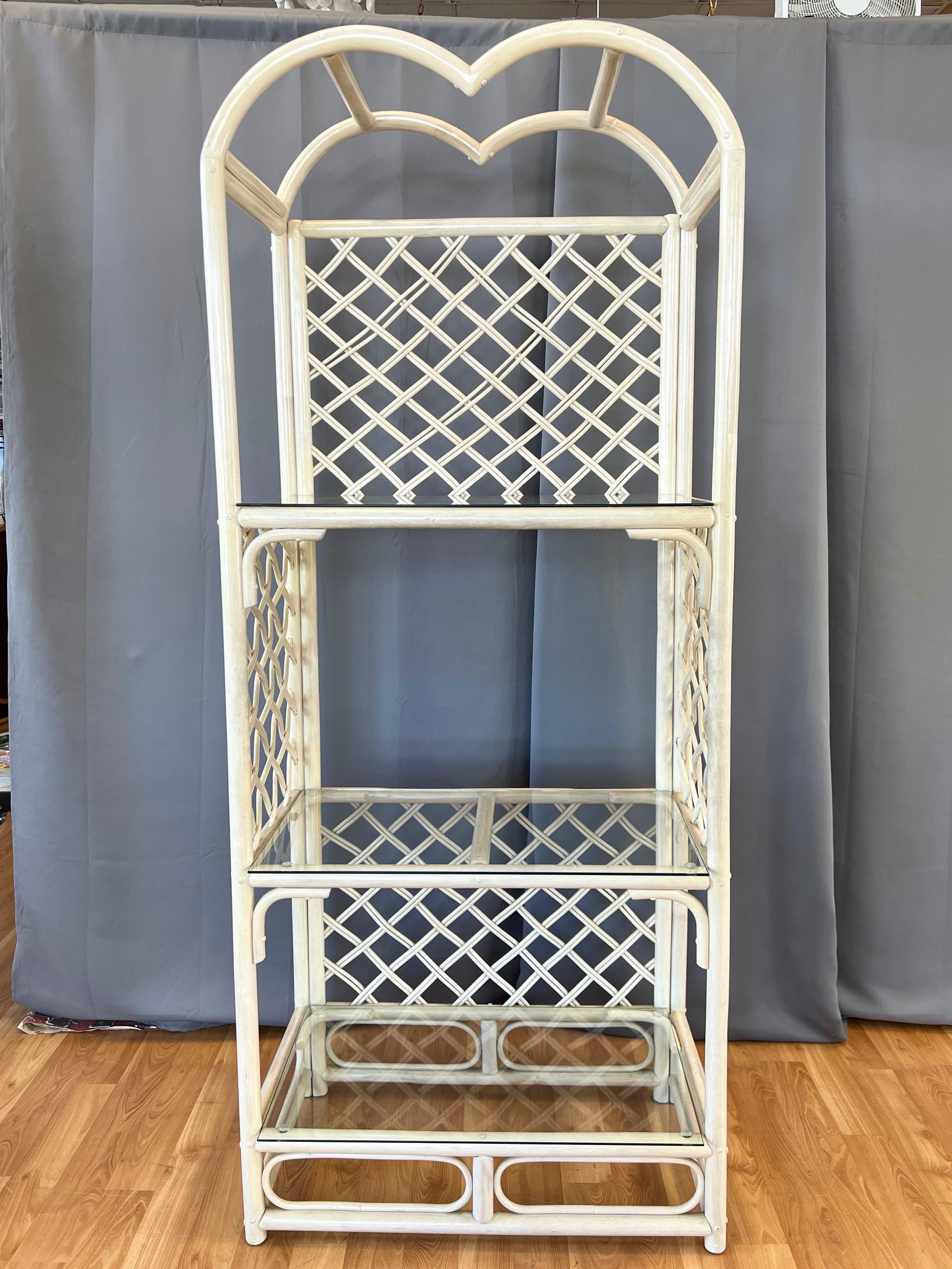 A tall and spacious late 1970s or early 1980s McGuire-style bent rattan étagère or shelving unit with three glass shelves.

Striking and uncommon double-arched heart-shaped top with various bent rattan elements and woven lattice panels at the back
