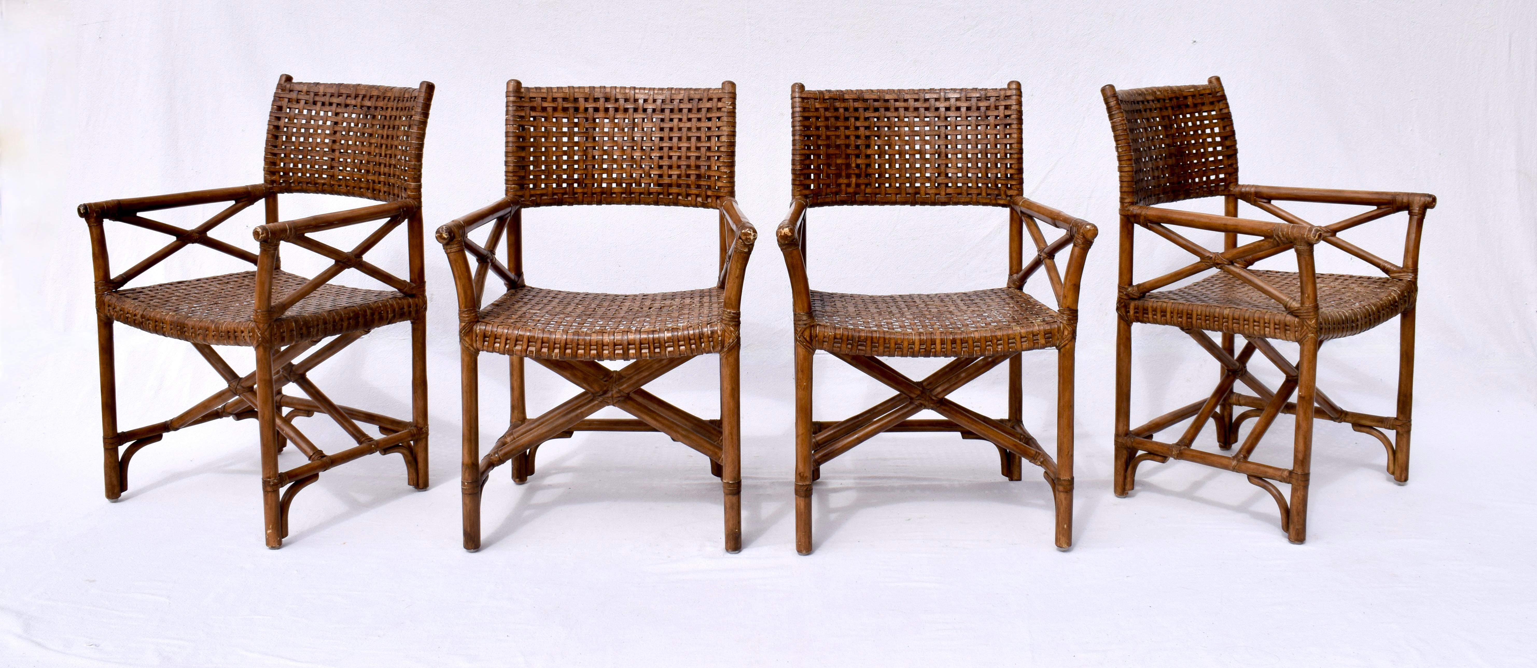 Set of four laced leather rattan dining chairs or armchairs made in the manner and style of McGuire. Director's style armchairs featuring woven rawhide seats and backs reinforced with leather strapping. Each has a beautifully distressed patina from