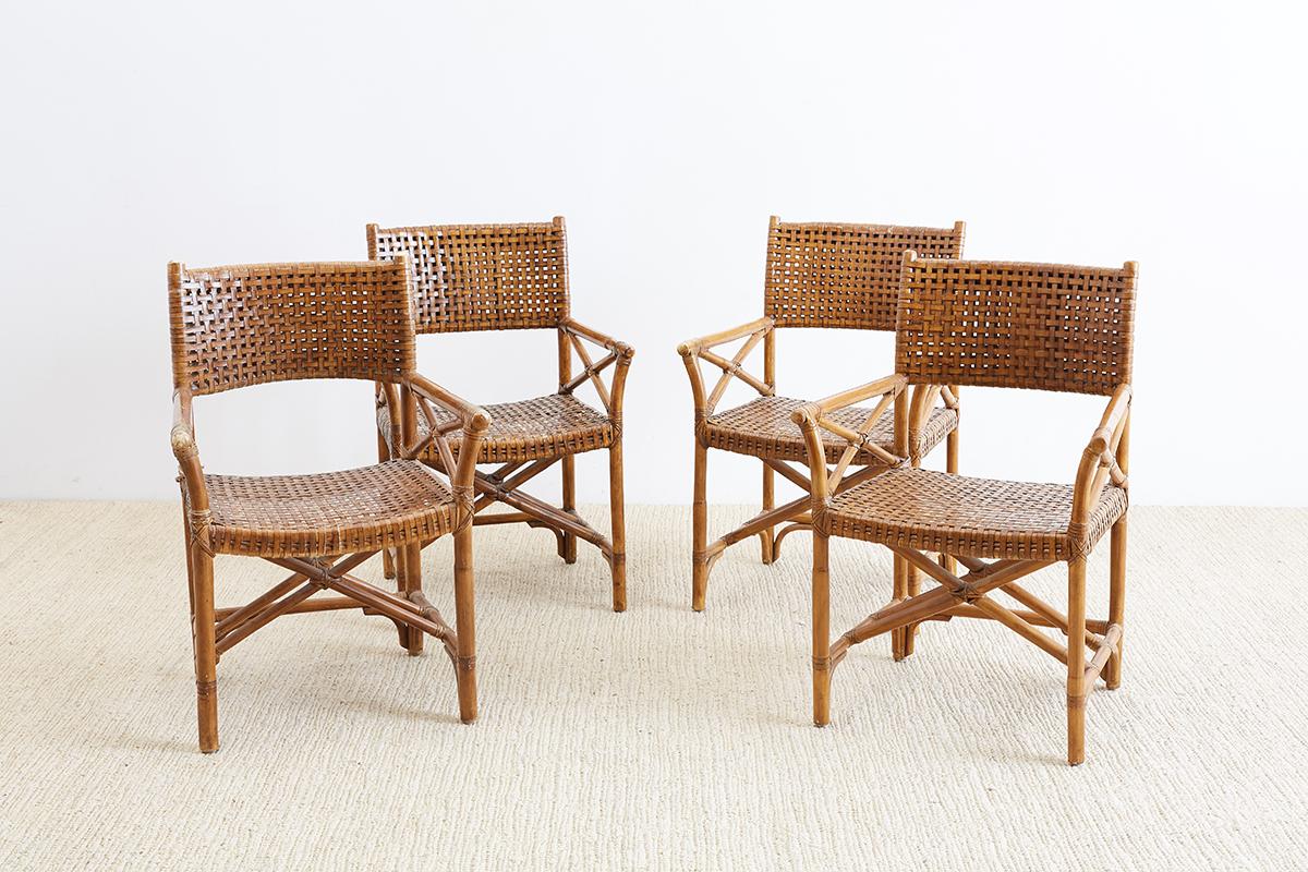 Set of four woven leather and rattan dining chairs or armchairs made in the manner and style of McGuire. Director's style armchairs featuring a woven seat and back reinforced with leather strapping. Each has a beautifully distressed patina from age
