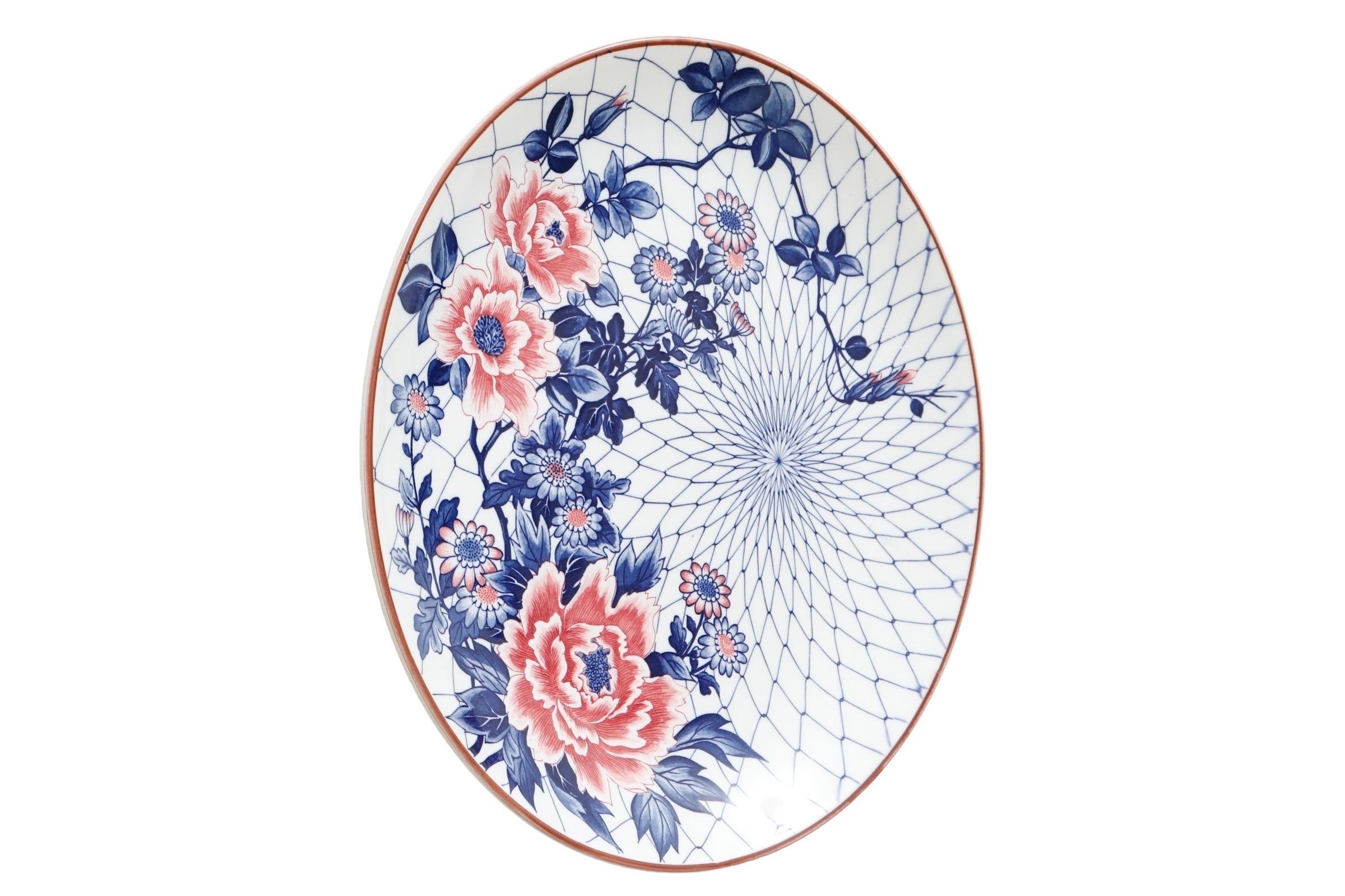 Un plat décoratif en transferware fabriqué au Japon vers 1940. Des chrysanthèmes rose vif et bleu cobalt grimpent d'un côté de l'assiette, avec en arrière-plan un motif de palmier décentré sur fond blanc. Labellisé avec le sceau du fabricant, le mot