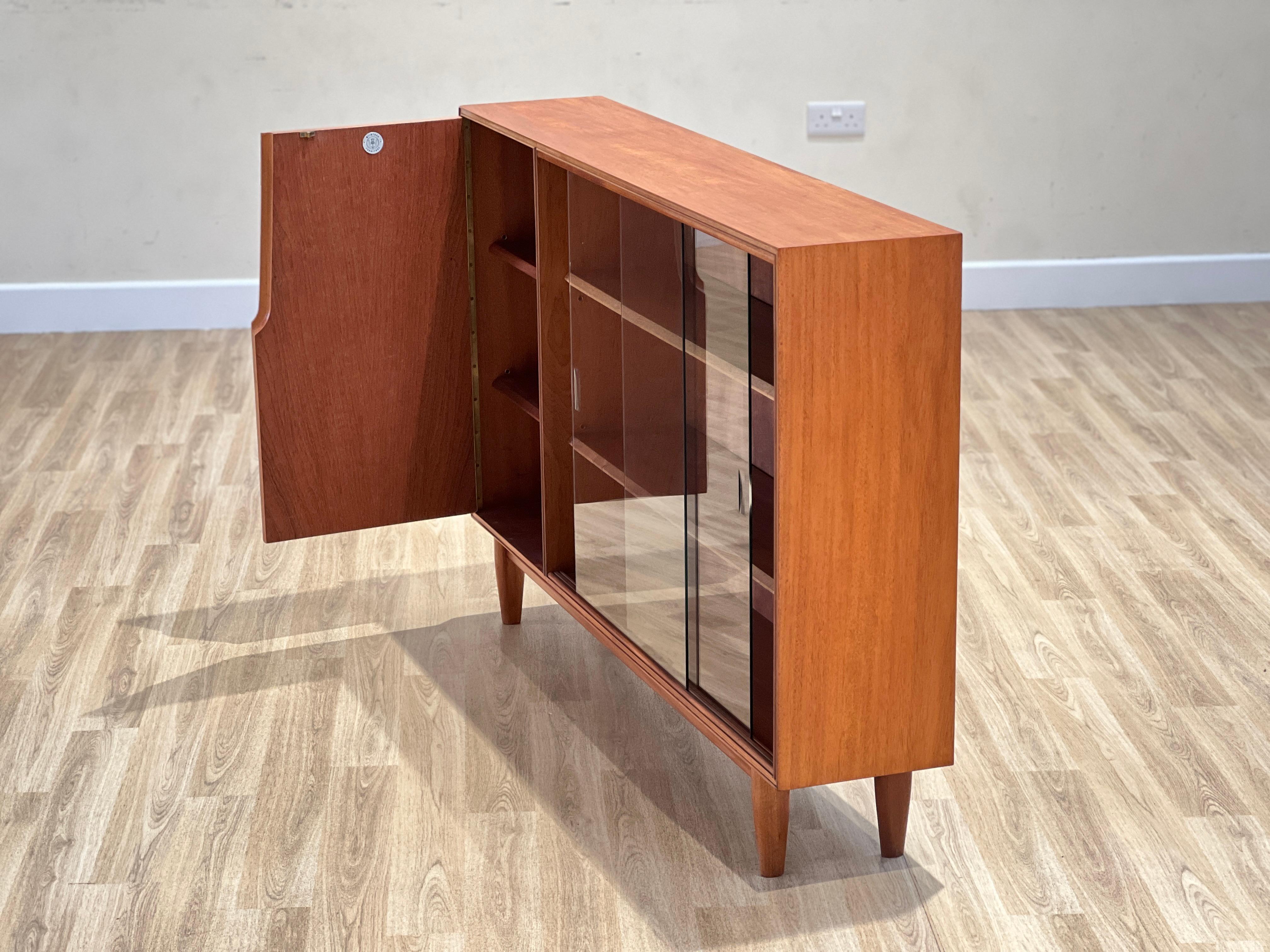 This exquisite display cabinet was created by Tom Robertson for the prestigious Scottish cabinetmaker A.H Mcintosh during the 1960s. It’s crafted from high-quality teakwood and features an elegant glass front panel.

The door on the left-hand side