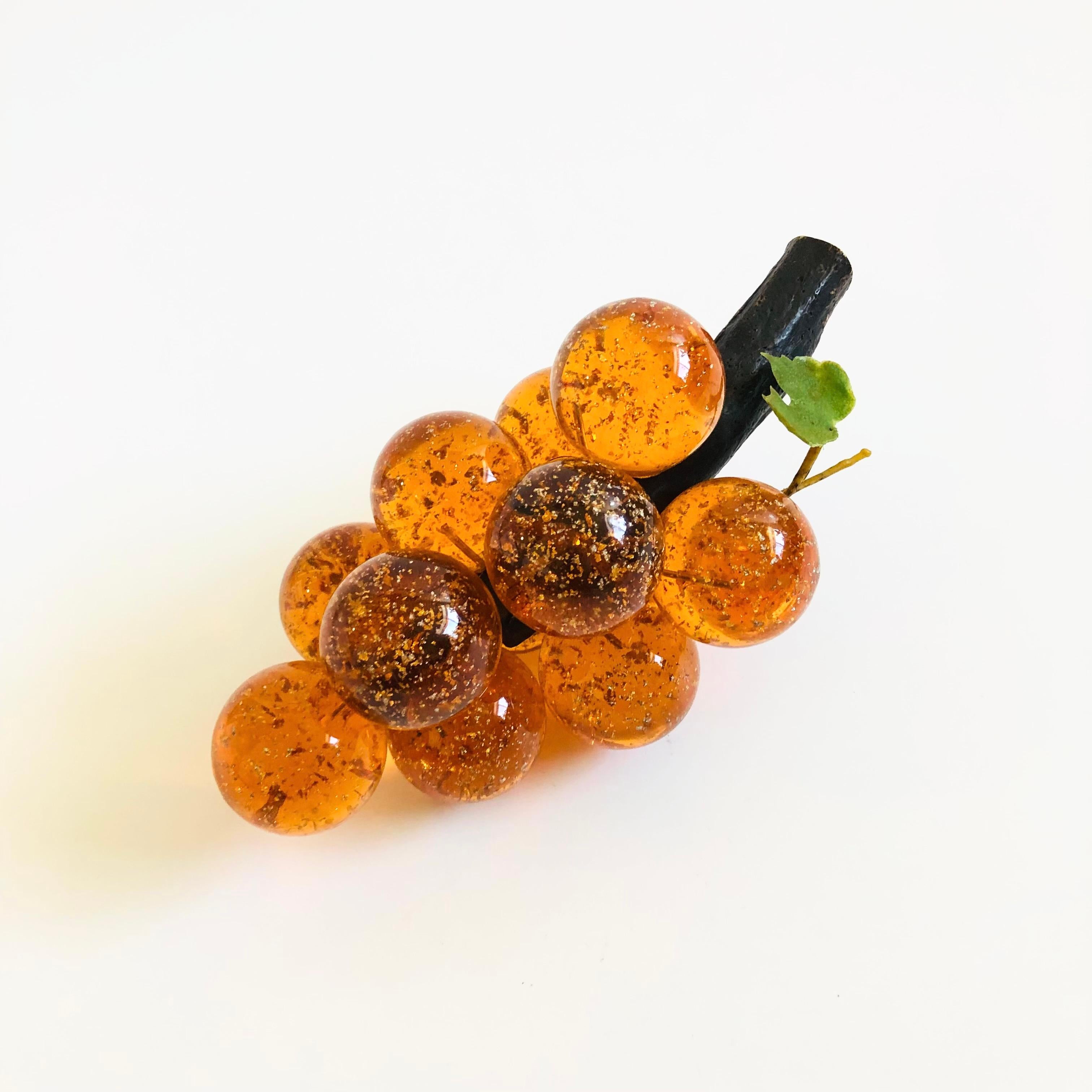 A mid century lucite grape cluster. Spherical lucite grapes are held together by metal wires. Fastened on a natural wood stem. Beautiful variation in the amber color of the grapes with gold glitter interiors. A great table top decorative piece.

