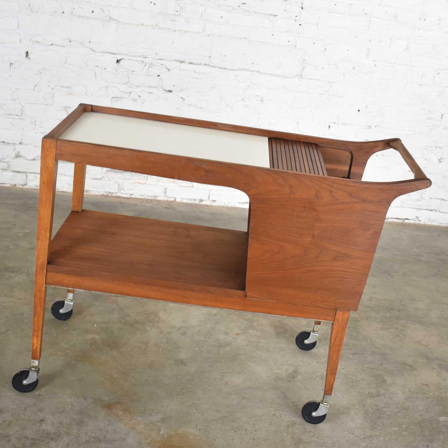 Handsome MCM aka Mid-Century Modern walnut and white laminate rolling server #3184, bar cart, serving cart, beverage cart, tea cart, or dessert cart designed by Arthur Umanoff for Cavalier Corporation’s Dimension Group. It is in wonderful vintage