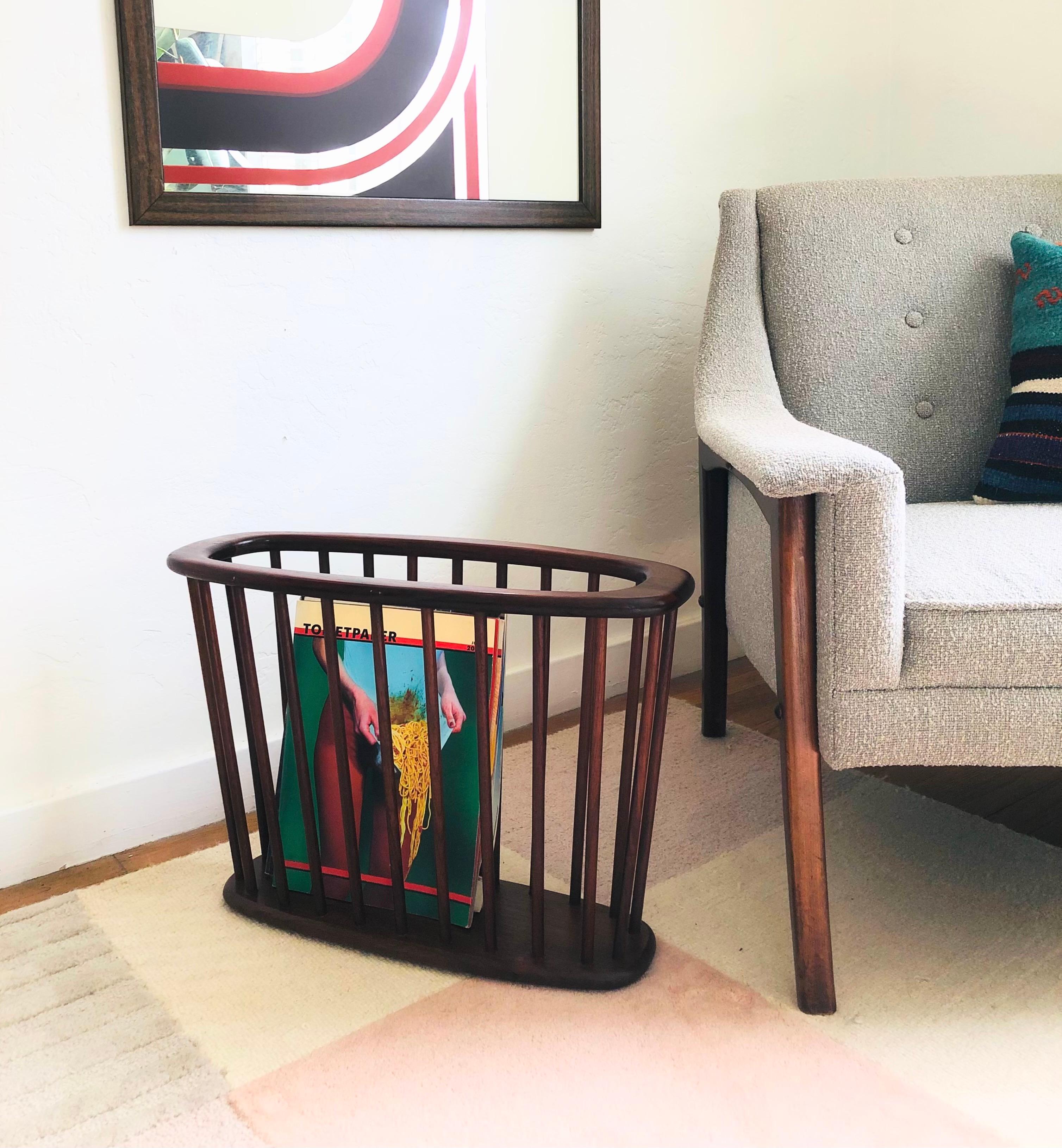 A mid century walnut magazine rack designed by Arthur Umanoff. Oval with vertical spindles around the sides. Elegant tapered shape. A wonderful mid century minimalist design and functional storage piece.

