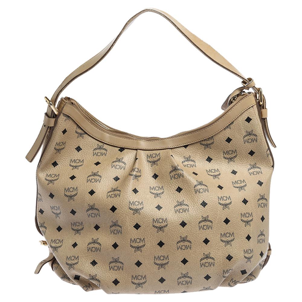 Diese umwerfend schöne MCM Hobo ist aus beschichtetem Canvas in Visetos in einem beigen Farbton gefertigt. Das Äußere zeigt das Markenlogo in Goldtönen und einen Schulterriemen. Der Reißverschluss an der Oberseite führt zu einem geräumigen