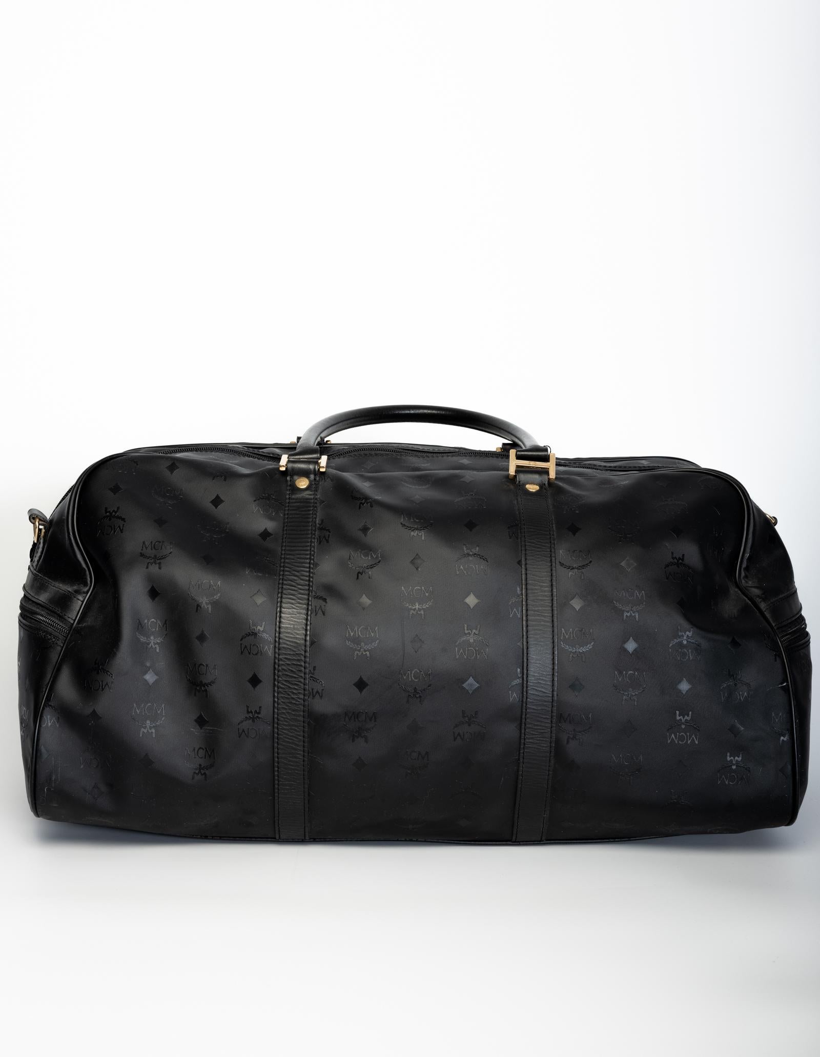 This MCM duffel bag is made of sturdy water resistant black nylon and features dual rolled leather top handles, a detachable shoulder strap, gold tone hardware, two exterior zipper pockets, an interior zipper pocket, and black woven monogram