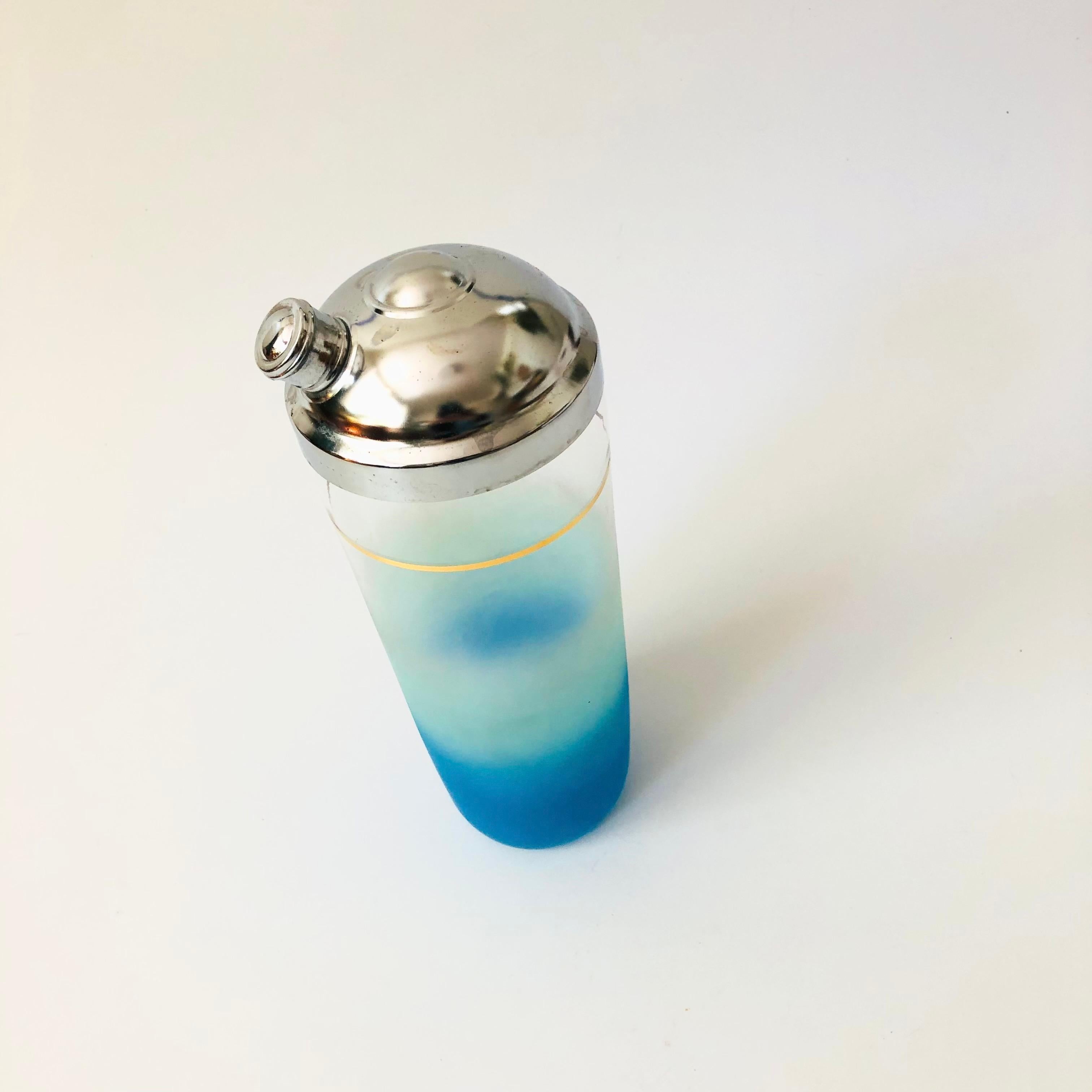A  mid century glass cocktail shaker. Beautiful blue blendo coloring to the glass the fades from bright blue at the base to clear at the top. A band of metallic gold decorates the upper part of the glass. Topped off with a chrome cap.

