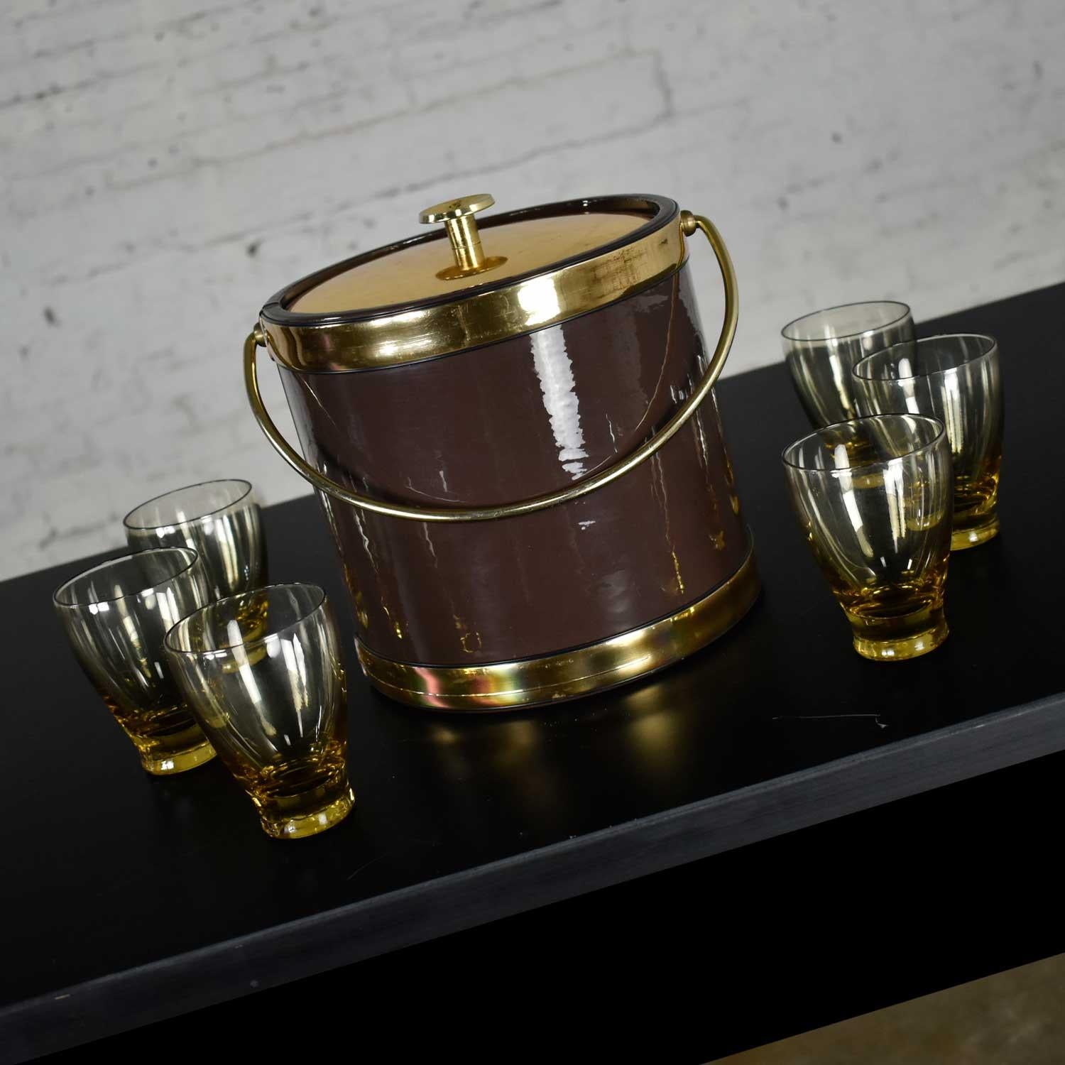 Awesome MCM Mid-Century Modern style set including a vintage brown vinyl ice bucket by Kraftware with gold detail and bail handle, brass plated lid, and knob, insulated plastic interior and six bar glasses in the style of Russel Wright. There are a