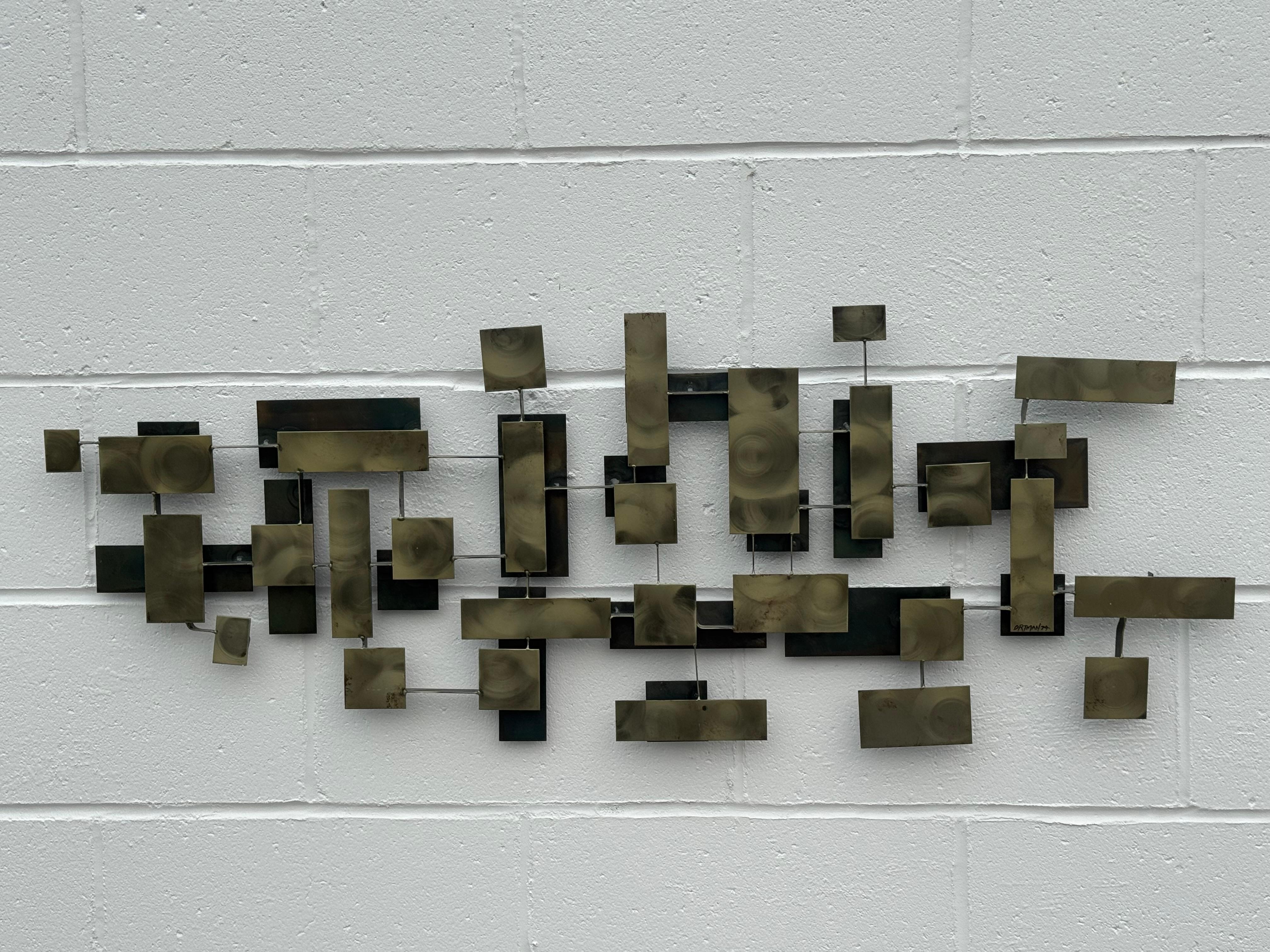 Grande scultura brutalista MCM in metallo appesa alla parete, circa 1974, dello scultore/artista di Riverside, California, J. Gaylord Ortman (1931-2021).  Costruito da pezzi quadrati di metallo rettangolari e sabbiosi, con volute e patine,