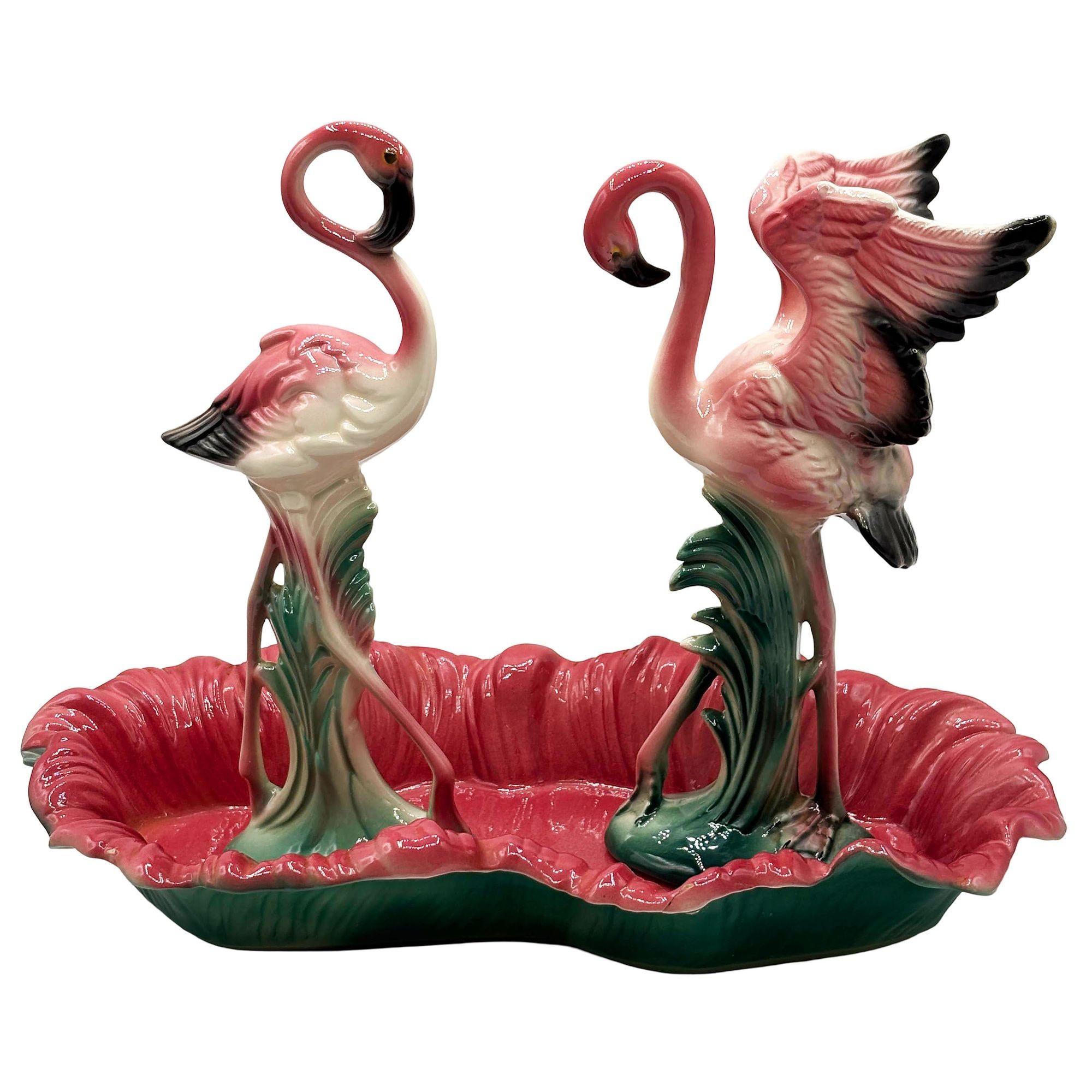 Mid-century set of 2 pink and green flamingo ceramic figurines with flamingo pool tray decorative bowl. The set features two beautifully detailed pink flamingos with their wings outstretched, set among lush green leaves, and a matching pool tray