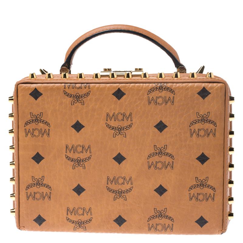 Adorned with decorative gold-tone studs on the exterior, this bag from MCM has a structured shape. The bag comes crafted from signature leather and flaunts a top handle and a shoulder strap. The trunk style bag opens to a suede-lined interior that
