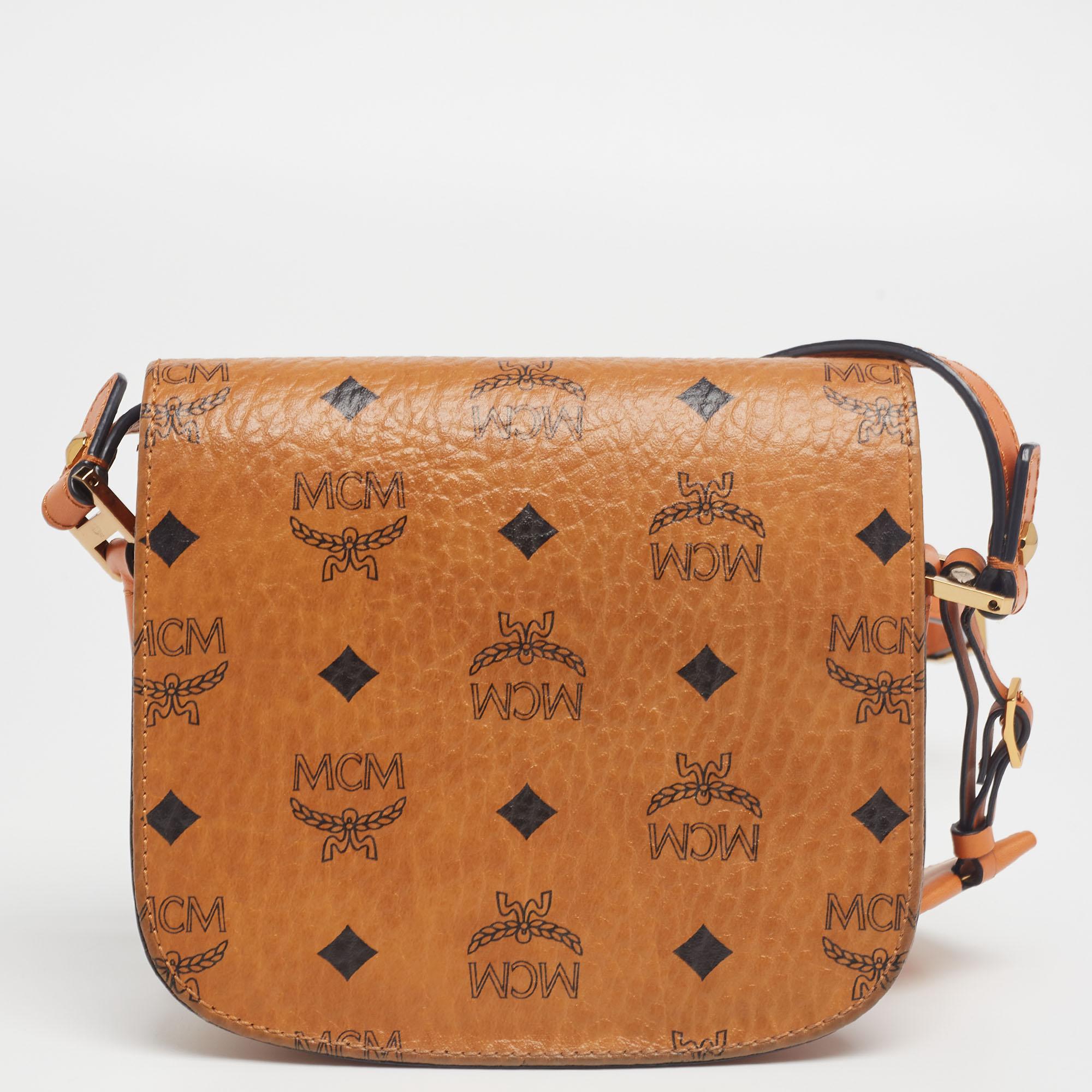 The design of this MCM bag utilizes Cognac Visetoes coated canvas and leather on its exterior. Lined with suede, the interior is equipped with two different compartments and a zipper pocket. The branded lock closure on the front envelop-styled flap