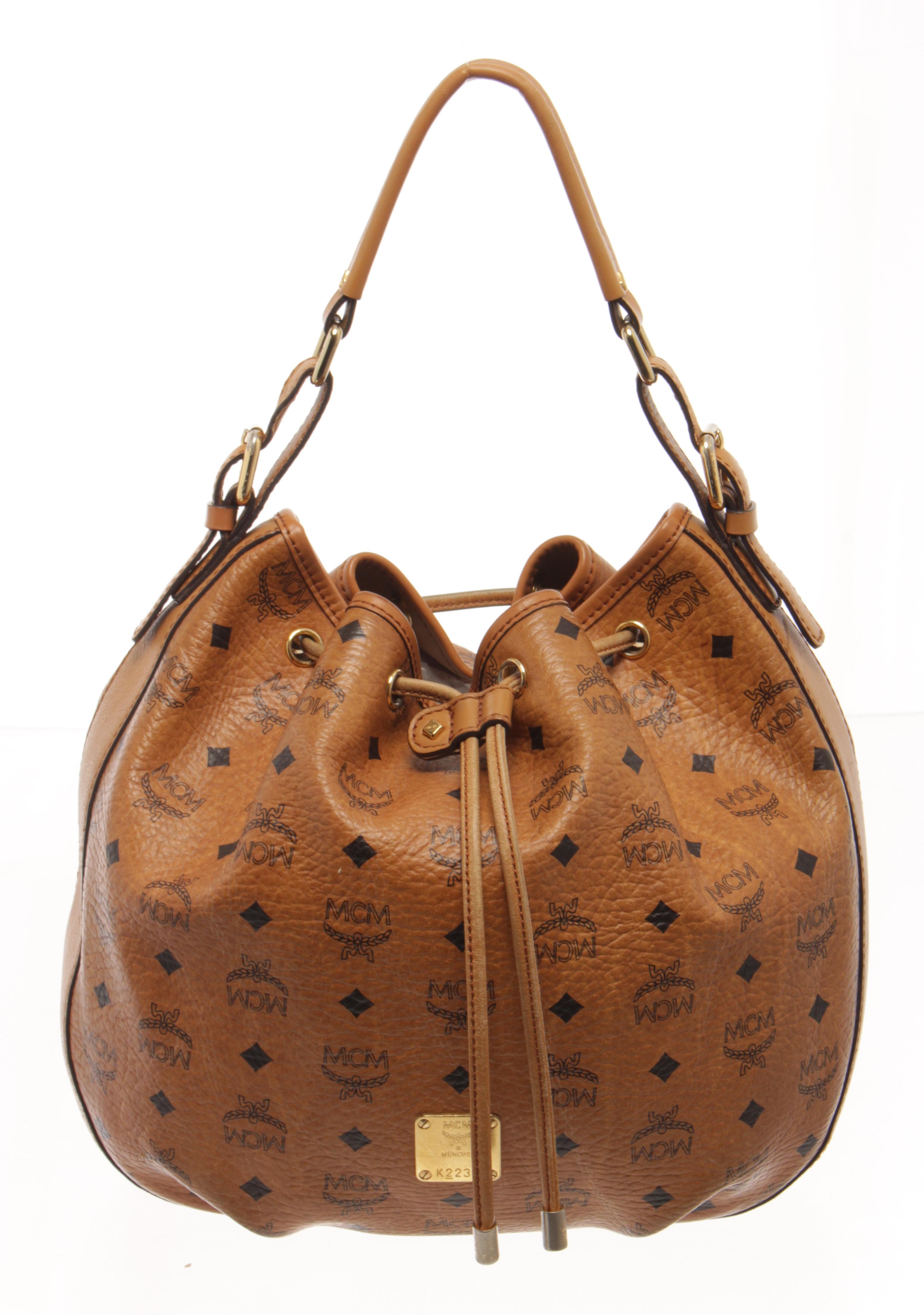 MCM Cognac Visetos Leather Bucket Bag with dark gold-toned hardware, interior side zip pocket and open pocket, visetos coated canvas and trimmed in rich nappa leather, drawstring fastening with concealed magnetic closure, removable top handle,
