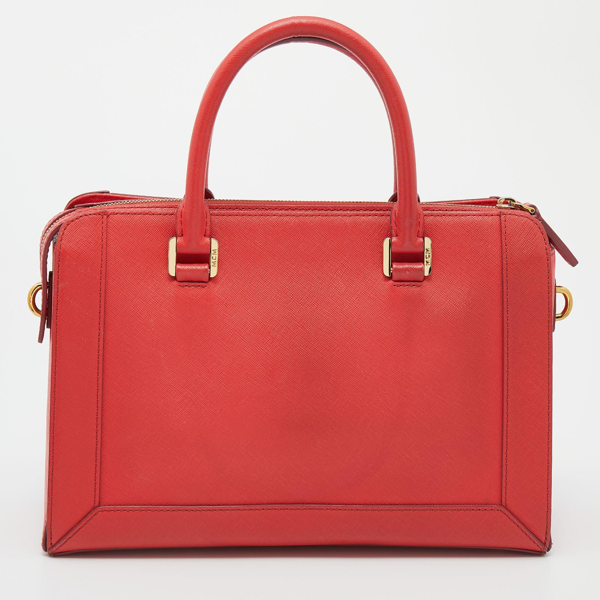 The MCM tote is ideal for those who commute daily, love shopping, and travel often. Made from coral leather, the creation is highlighted with a front brand plaque and attached with short top handles and a shoulder strap. The spacious interior makes