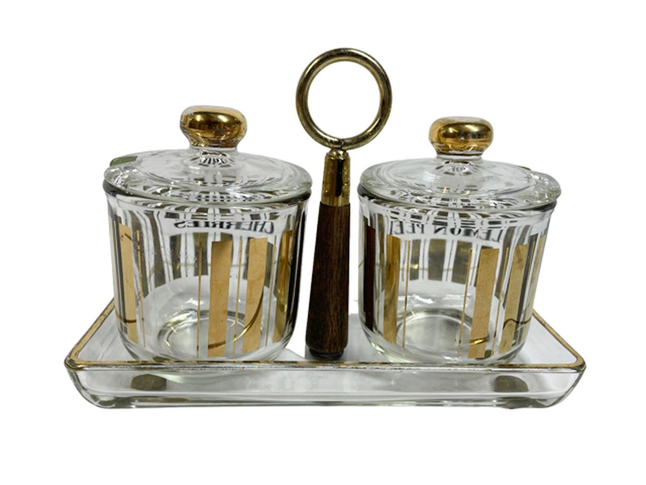 Hard to find, pair of mid-century modern garnish jars in a rectangular glass tray with central metal ring toped wood handle. the jars decorated with gold vertical bars and labeled in black for 