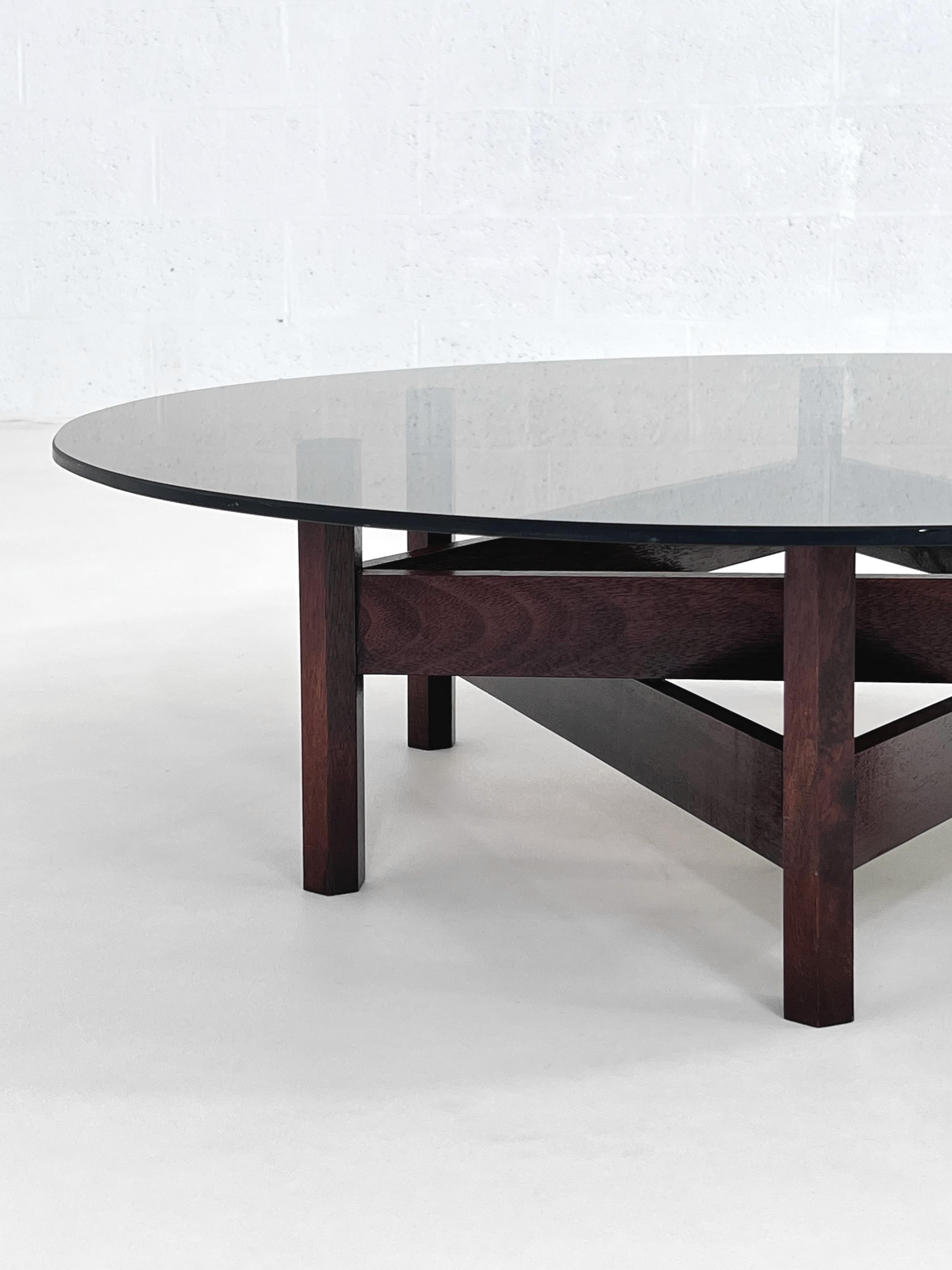 MCM Design Round Glass Top And Star Wooden Base Coffee Table composed of a large round and smoked glass top with a star shaped wooden base.