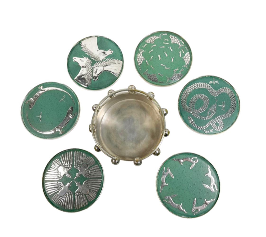 Six mid-century modern Mexican silver drinks coasters. Each coaster of a silver plate base and rim with a matte green ceramic surface, each inlaid with stylized silver animals. The six coasters in a silver plate galleried holder.