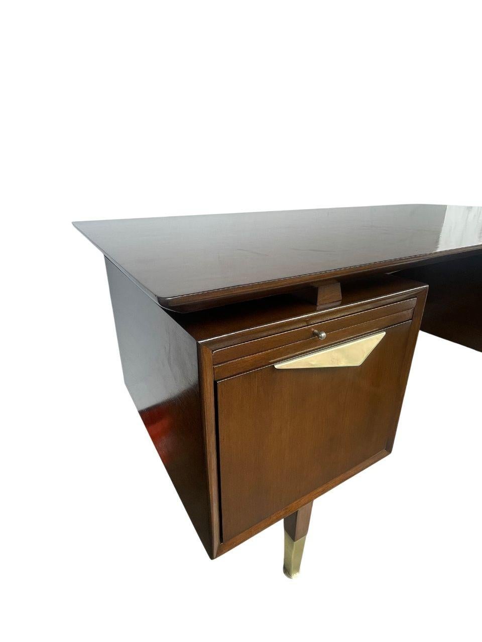 A striking MCM Danish executive desk from the 1960s, expertly crafted from rich walnut and featuring a sophisticated floating top design. The desk is accented with elegant brass details and cane-paneled, blending natural textures with refined