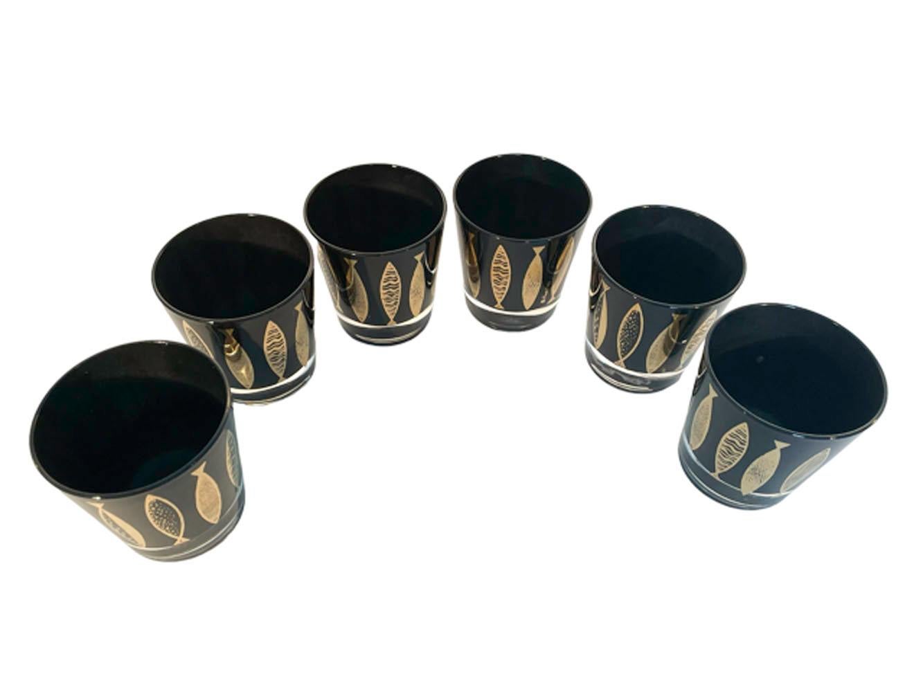 Six Mid-Century Modern old fashioned glasses designed by Fred Press, with 22k gold fish in different abstract patterns, vertically placed around each glass. The glasses are clear glass with the interiors frosted black creating a high gloss