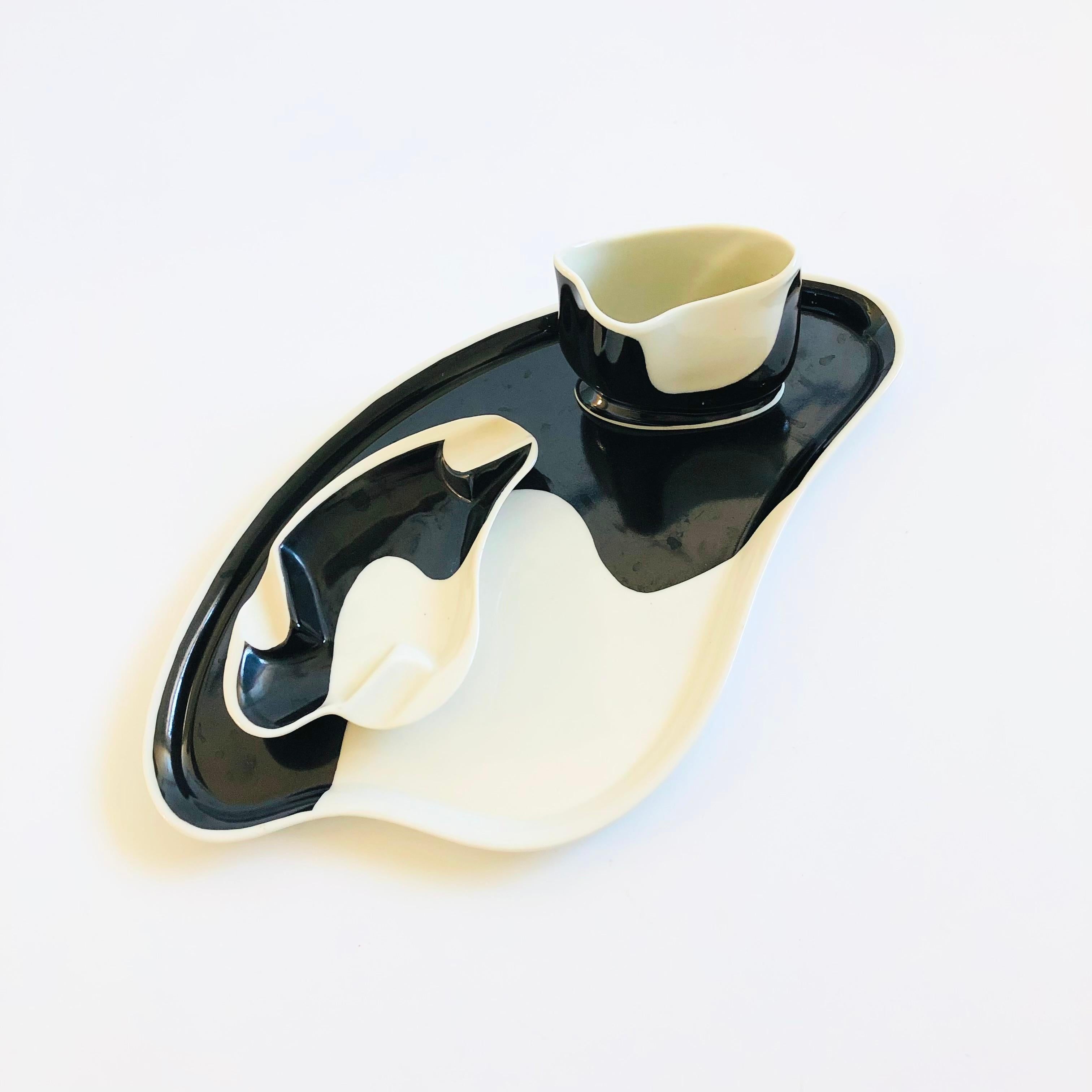 A set of 3 mid century German porcelain dishes. Each in a unique organic shape and finished in black and white glazes. The set includes a large tray, and ashtray, and a cup. Marked 
