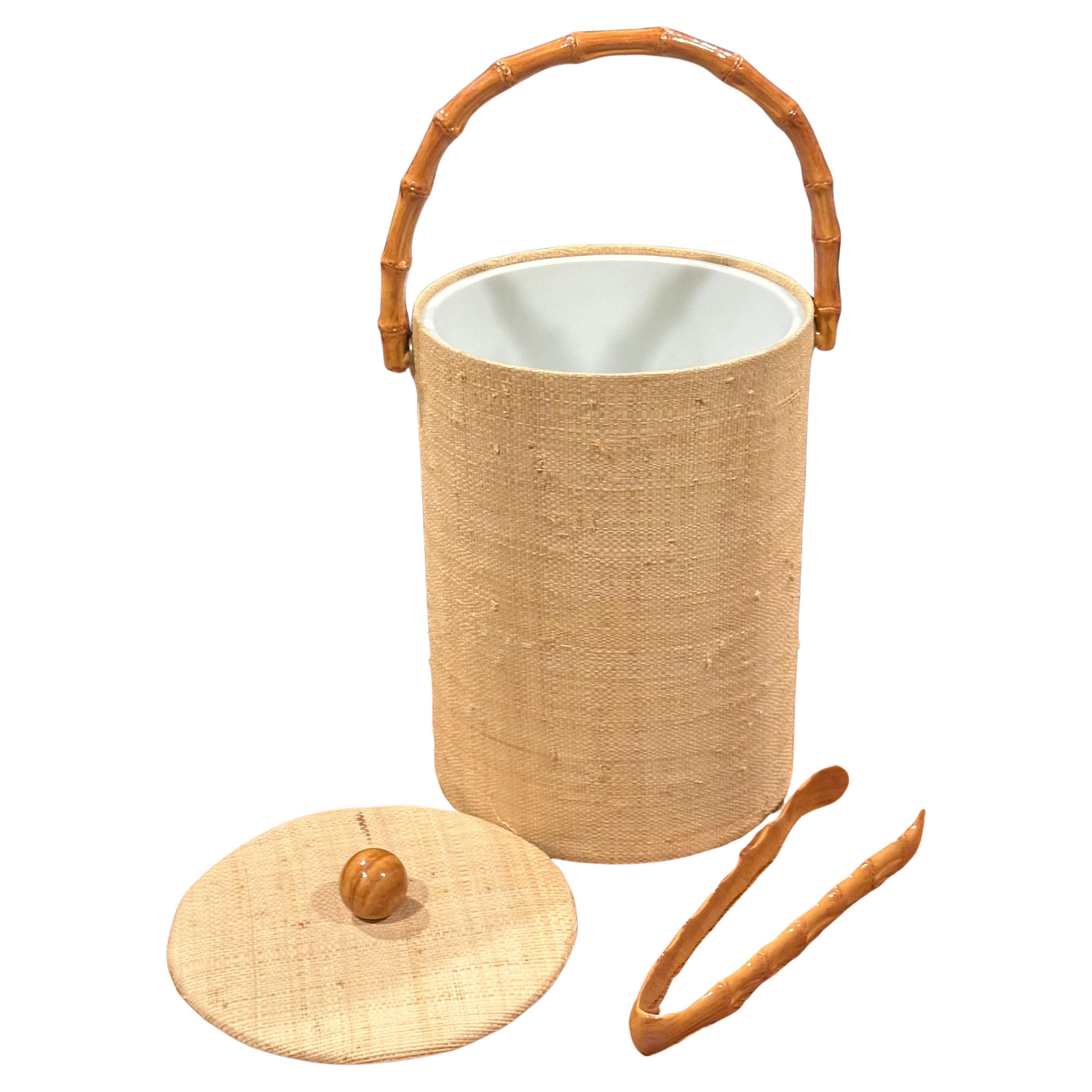 A very nice MCM grass cloth and bamboo ice bucket with tongs, circa 1970s. The set includes a pair of bamboo ice tongs and is in very good vintage condition; it measures 7.5