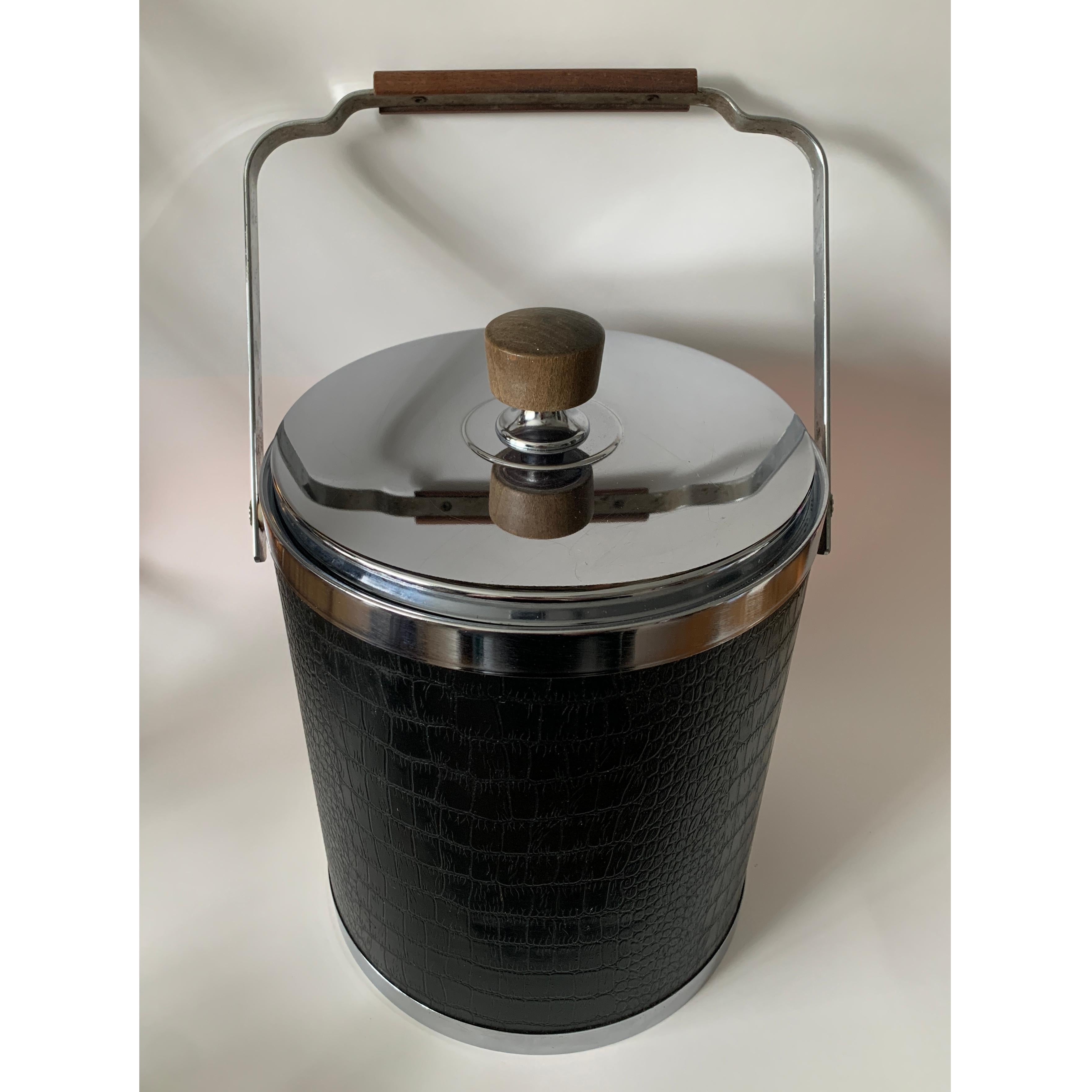 Vintage MCM ice bucket by Kromex

This chrome ice bucket is a cool as the ice it handles; with wooden handles and decorated in true 1960’s fashion with faux black leather crocodile print

Measures approx 11” high (not including handle) x 8 ¼” in