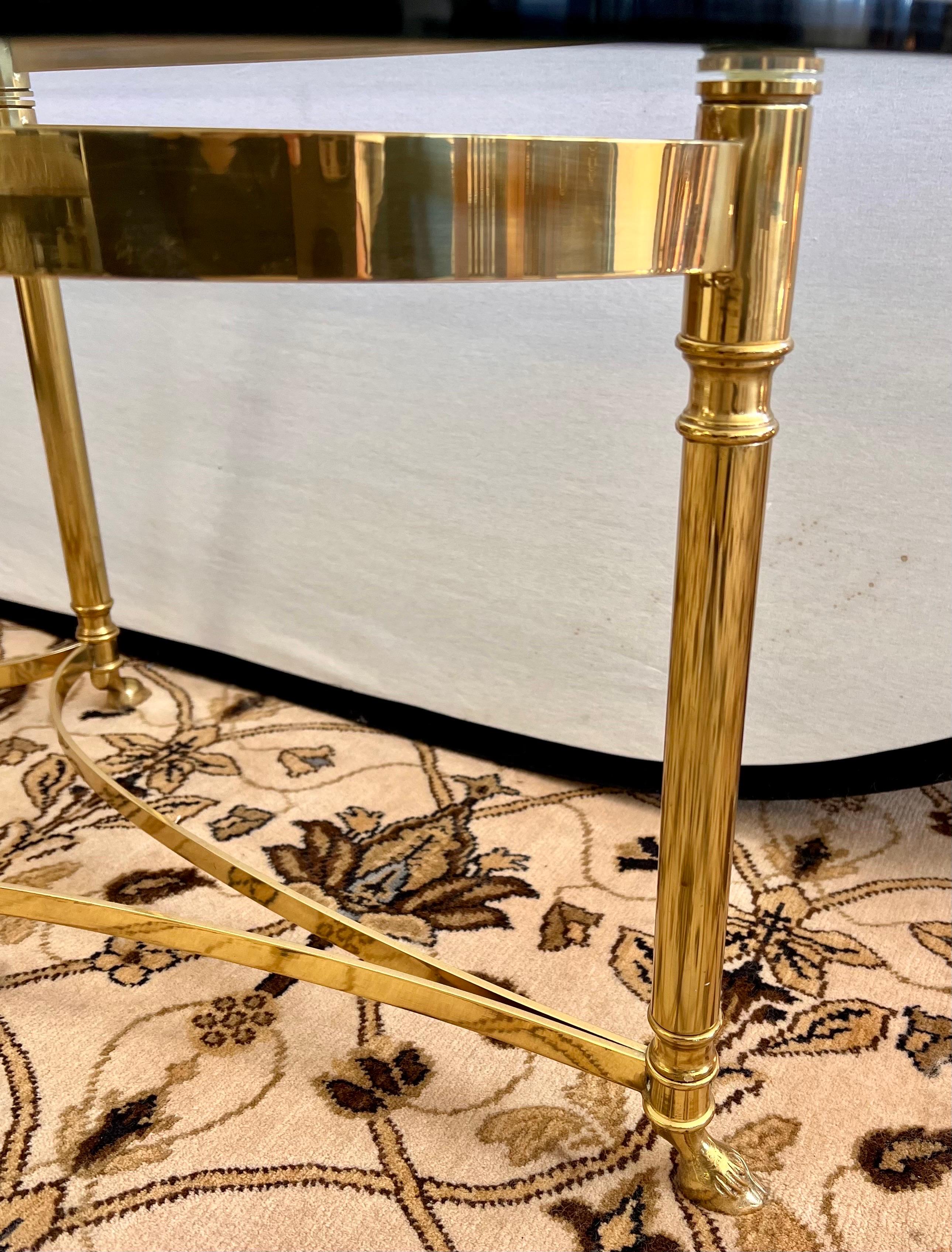 Stunning Mid-Century Modern cocktail table with elegant solid brass base and stretcher with hoof feet that supports an oval beveled glass top. Belongs in Architectural Digest!