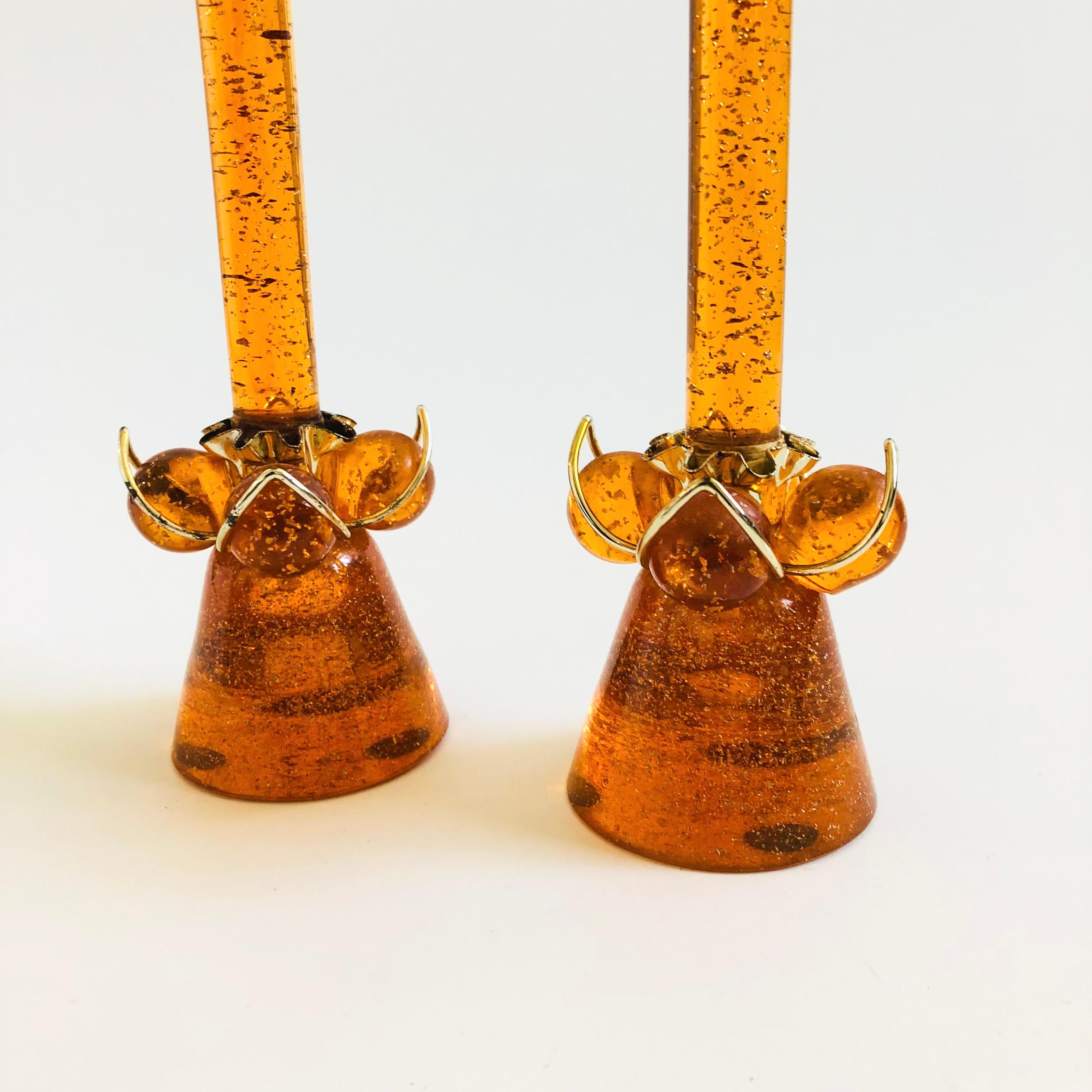 A set of 2 mid century lucite candle holders with matching flameless lucite candles. Vibrant orange color to the lucite with gold foil flakes to the interiors. Brass accents to the candle holders. The decorative candles can be removed for using with