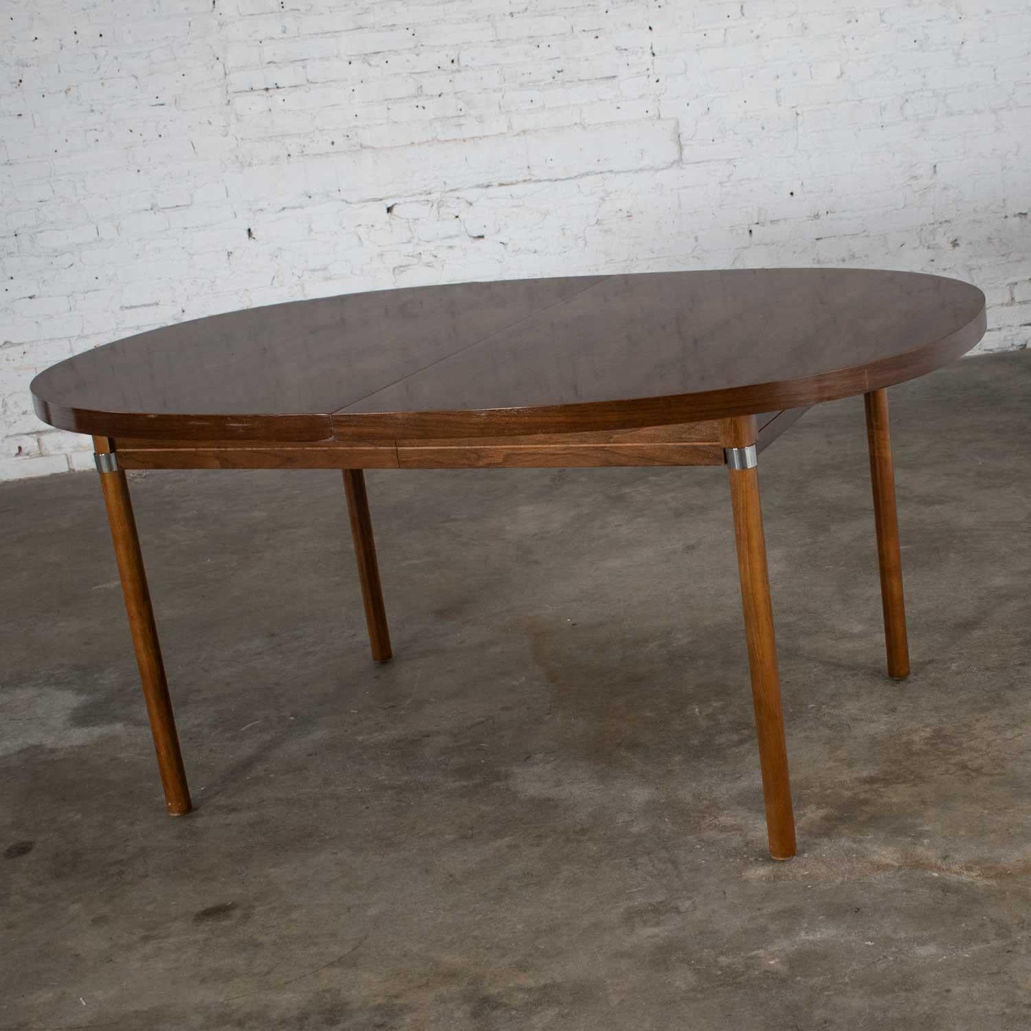 Beautiful oval Mid-Century Modern walnut toned expanding dining table with chrome accents, a wood grain laminate top, and one leaf. Wonderful vintage condition with a few minor touch ups as you would expect with wear and age. Please see photos.