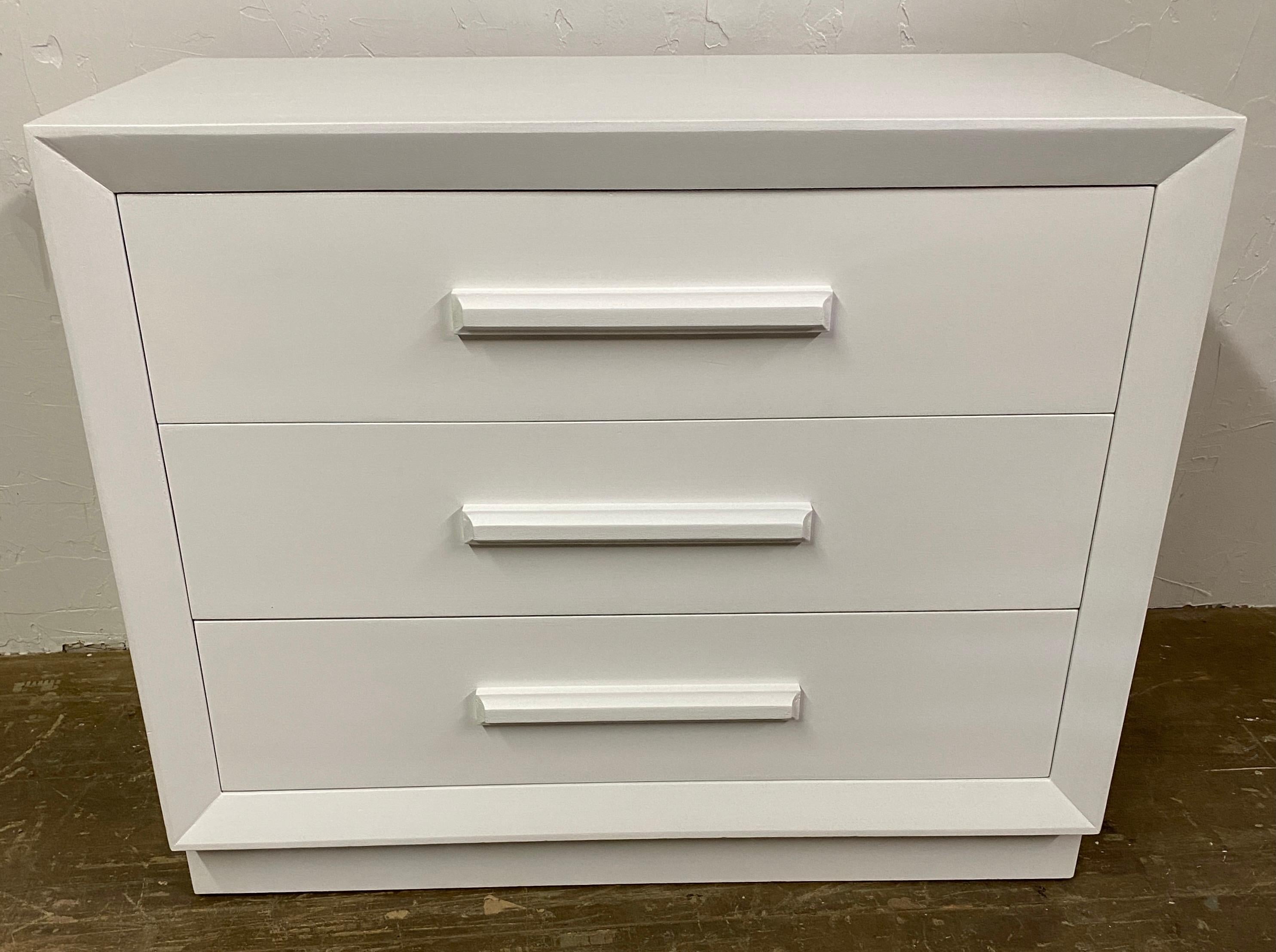 This Mid-Century Modern chest of drawers by John Stuart Inc of New York and Grand Rapids has been newly painted and restored. This piece features lacquered white paint with three pull out drawers, all three opens and closes with ease. This