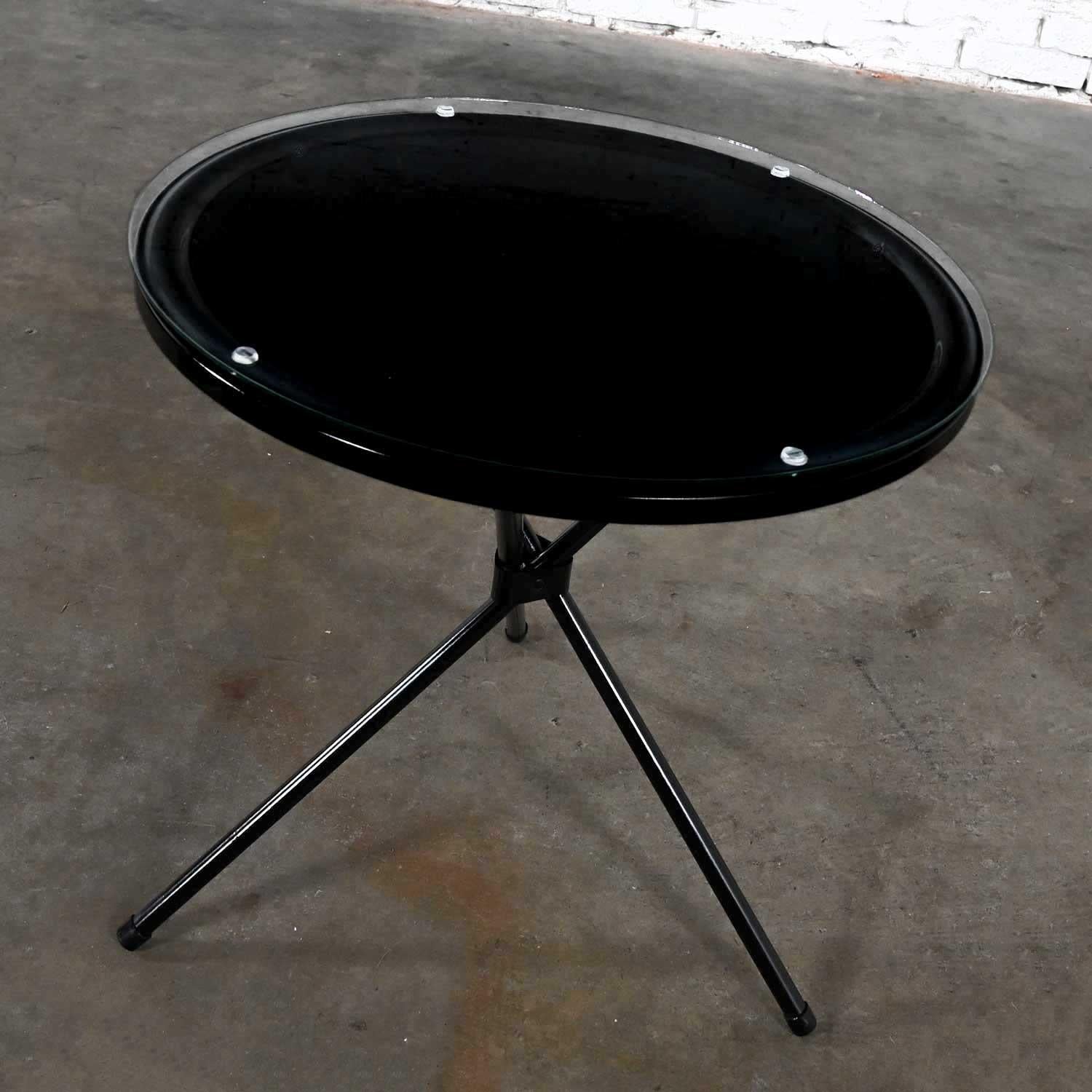 Spectacular vintage MCM (Mid-Century Modern) round black painted metal indoor/outdoor accent table with tripod base and glass top. Beautiful condition, keeping in mind that this is vintage and not new so will have signs of use and wear. We have