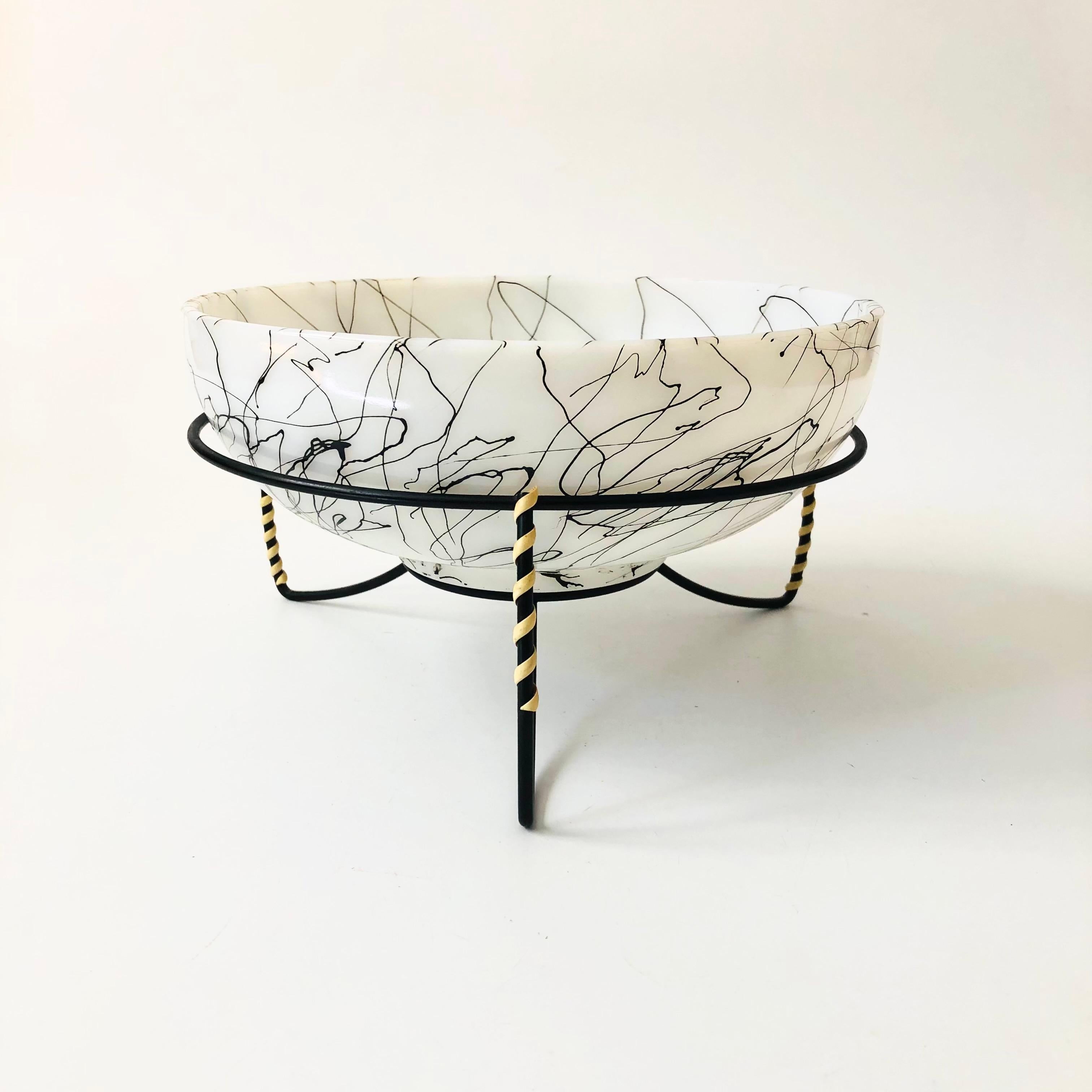 A large mid century glass salad bowl by Hazel Atlas in the spaghetti drizzle pattern. Made of white milk glass with abstract drizzle lines in black. Comes with a black metal stand with wrapped raffia detailing. A nice large serving piece perfect for